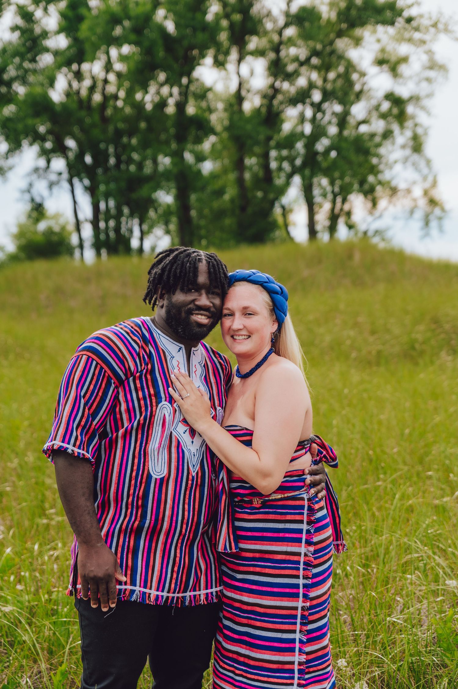 Couple in matching striped outfits embracing in a sunny meadow.