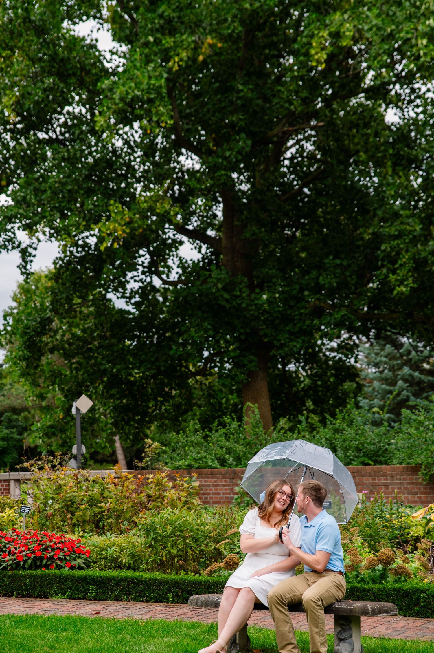 A romantic couple shares tender moments in a lush garden setting while holding a white umbrella.