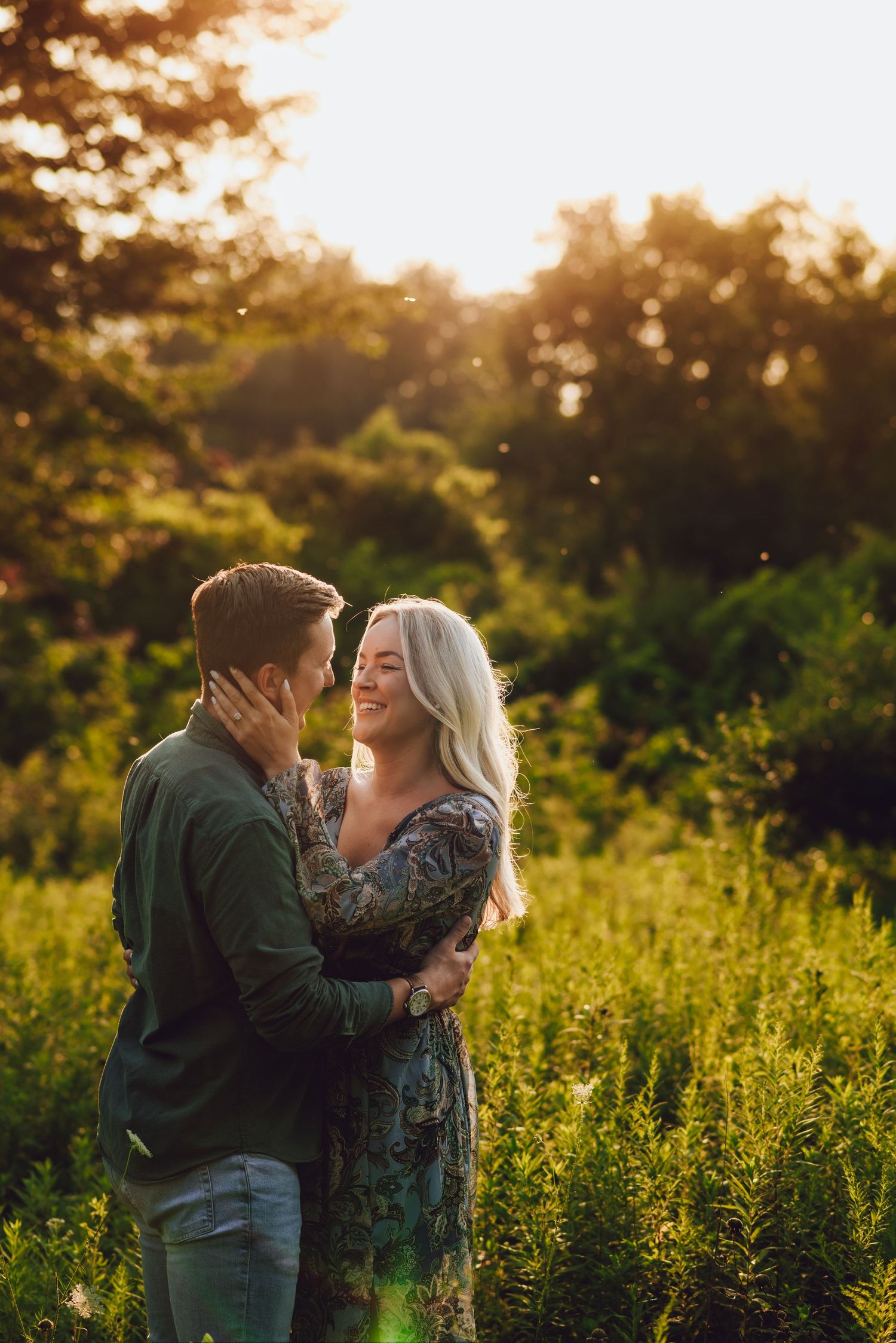 Romantic couple embracing in lush field during golden hour sunset.