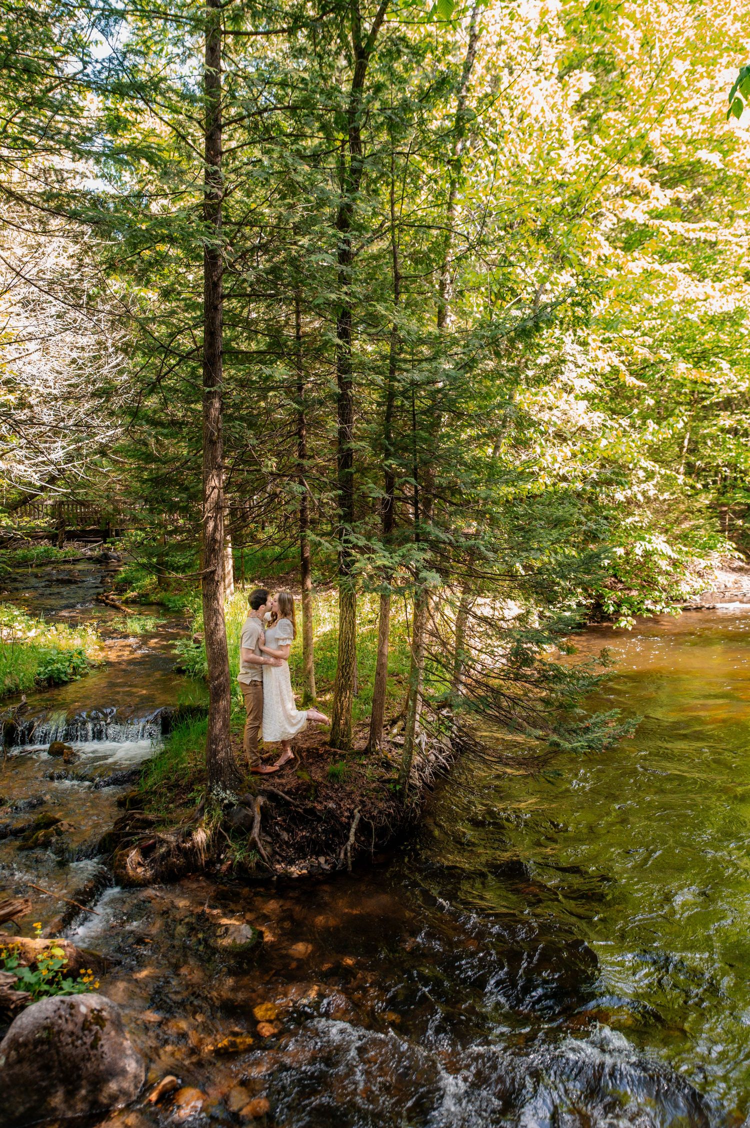 A person in a white dress stands on rocks near a cascading forest waterfall.