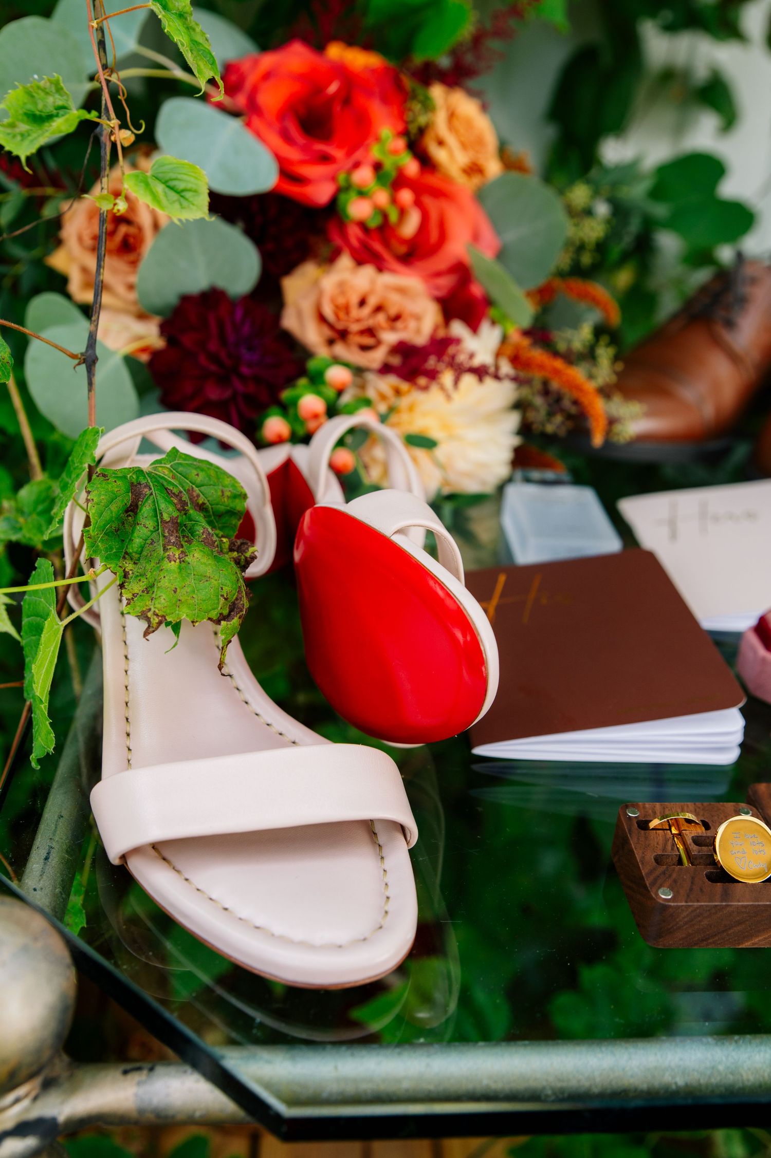 Beautiful red and pink floral arrangement nestled beside a white leather sandal in a garden setting.