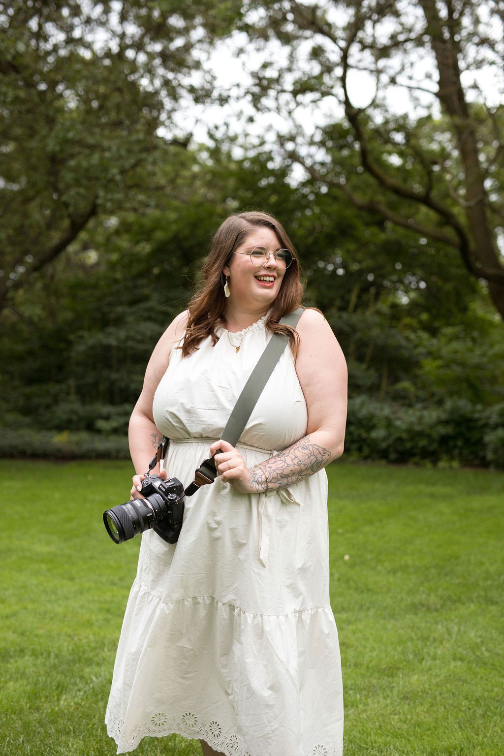 A person in a white wedding dress spins joyfully in a grassy outdoor setting during a photo session.