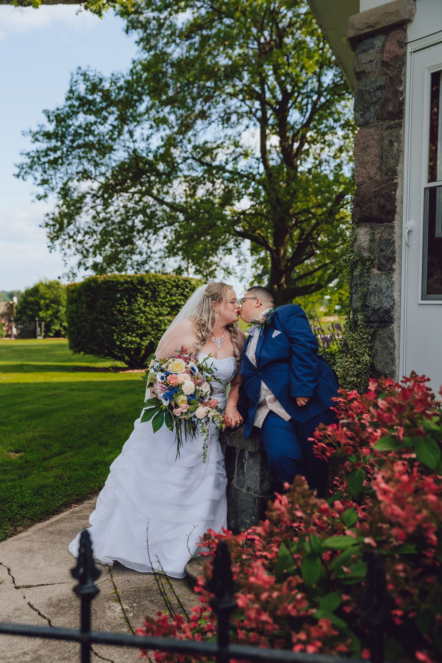 A romantic wedding couple shares intimate moments against a stone wall with red foliage in the foreground.