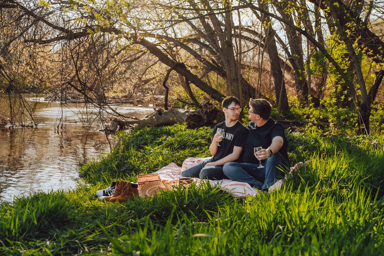 A riverside picnic setup with a couple relaxing on a blanket in dappled sunlight.