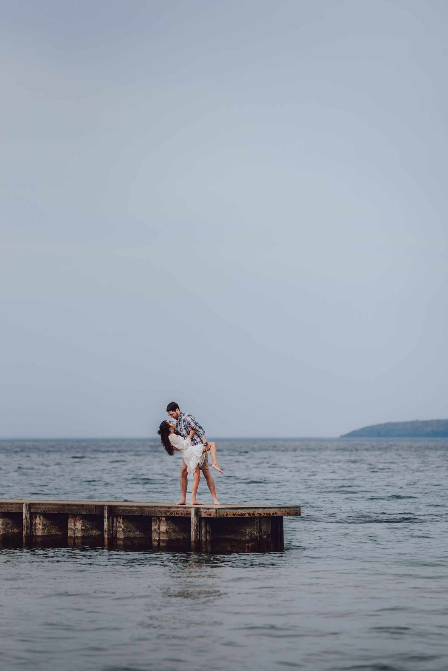 Romantic embrace on wooden dock overlooking misty ocean and distant shoreline.