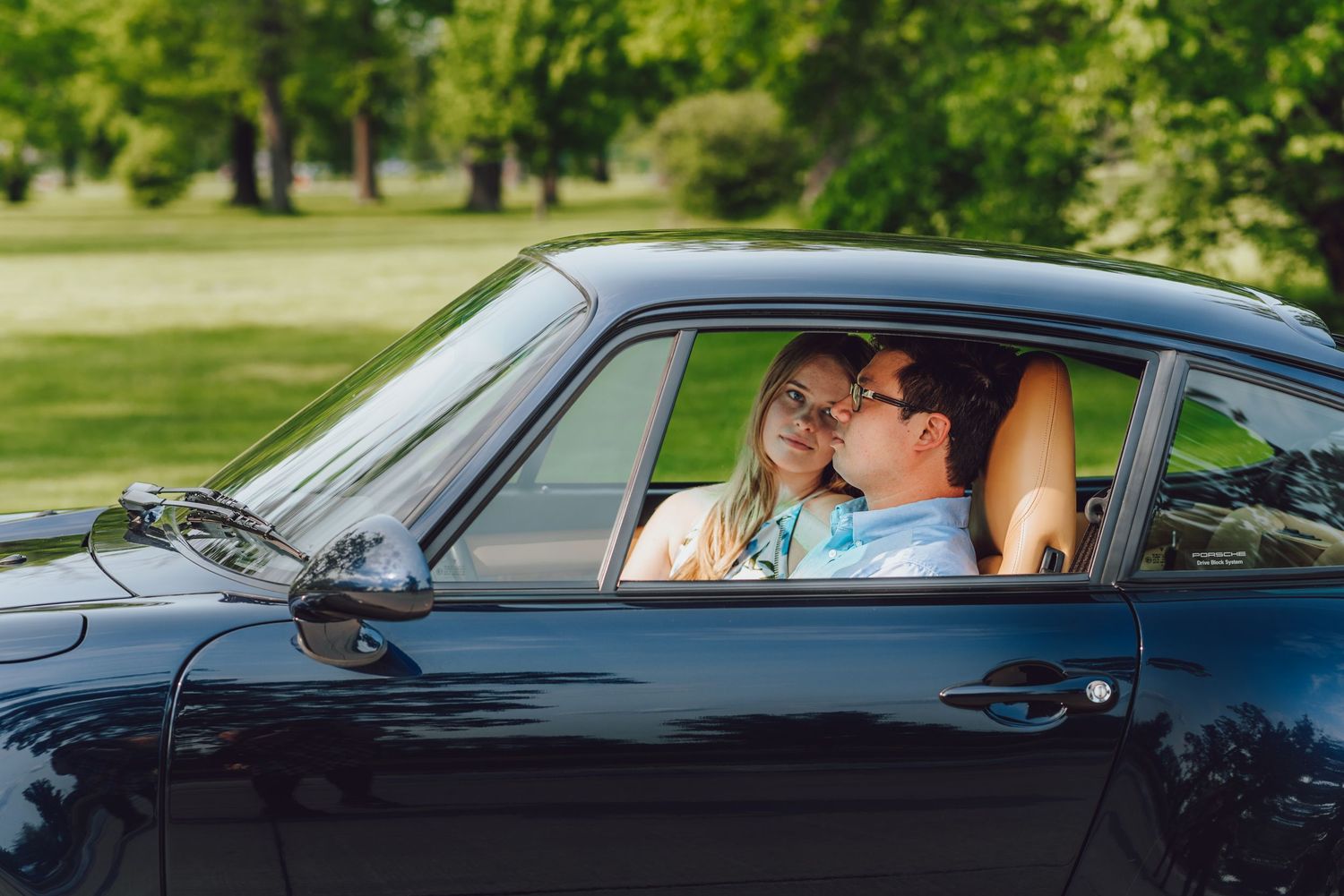 A couple sharing a tender moment inside a vintage black sports car.
