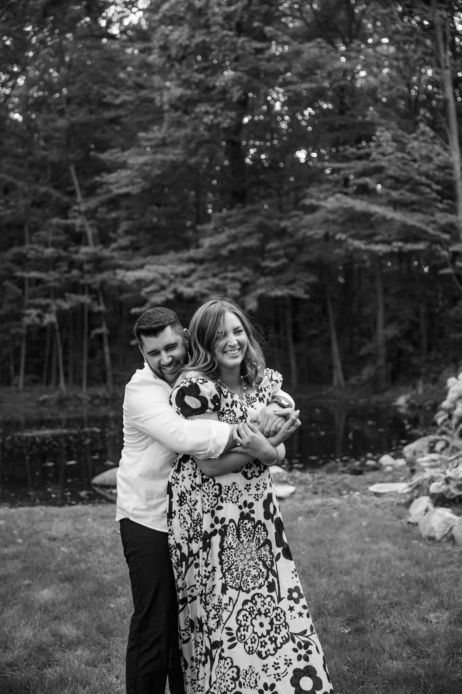 Black and white photo of a couple dancing together outdoors in a backyard with trees in the background.