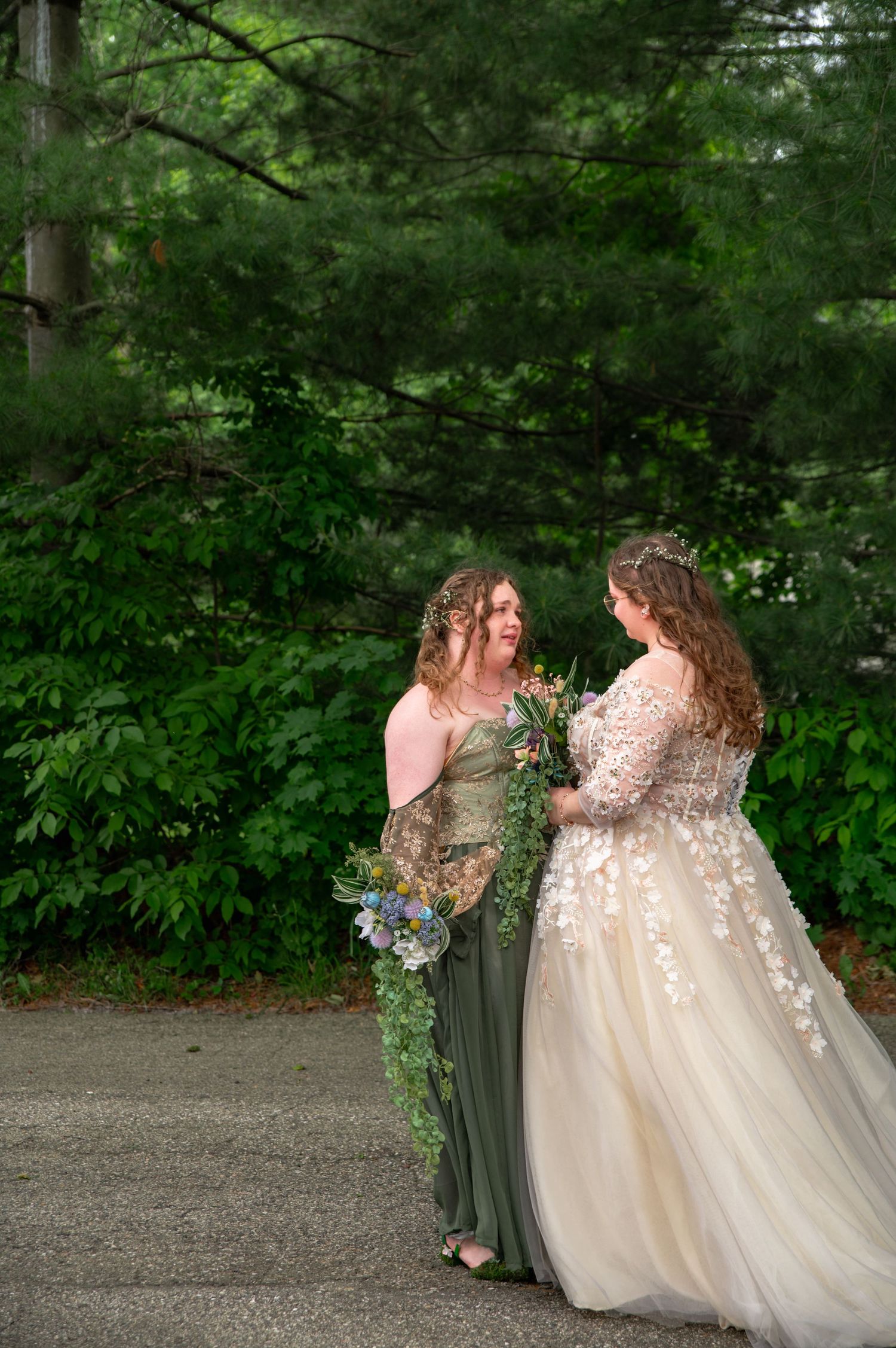 A joyful wedding party in a green outdoor setting shares laughter and embraces while wearing sage bridesmaid dresses.