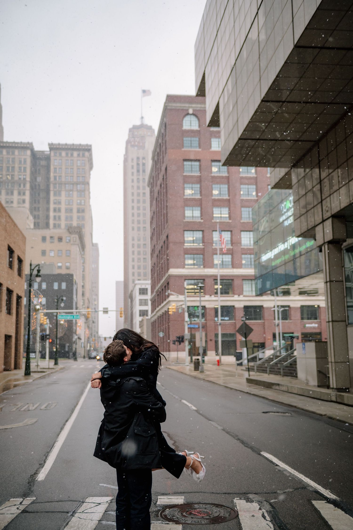 A loving couple embraces in the middle of a city street on a snowy day.