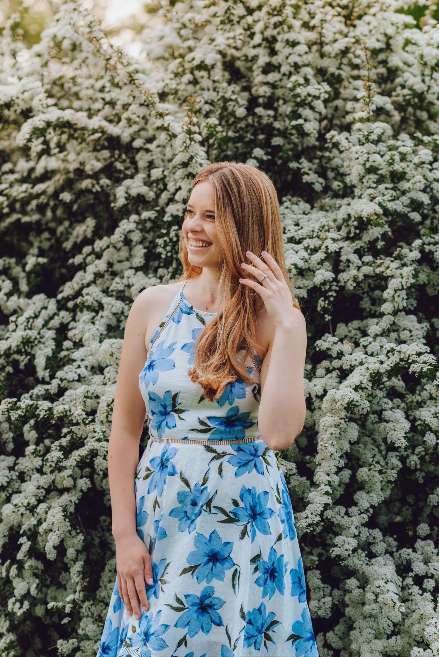 Woman in a blue floral dress standing against blooming white spring flowers.