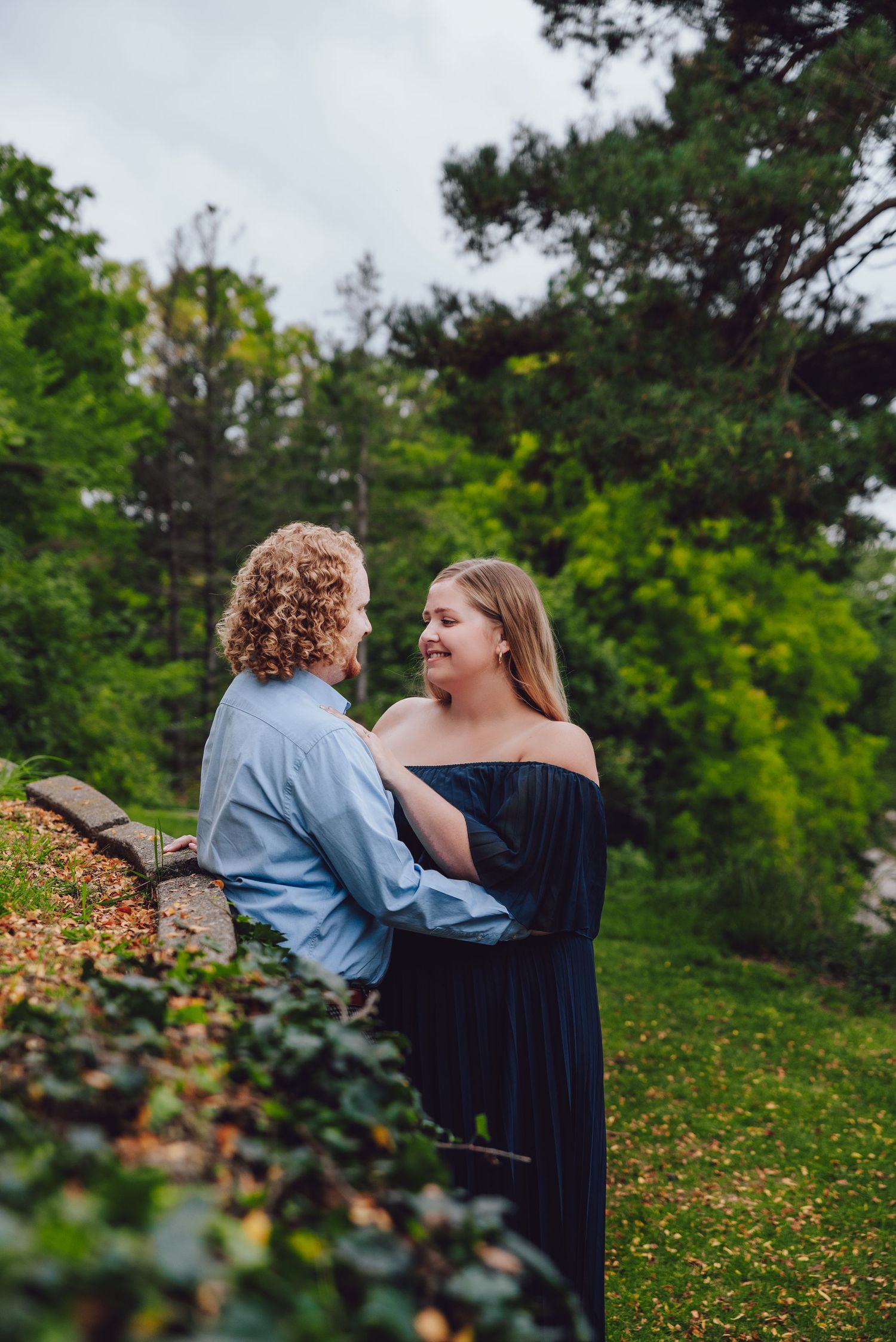 Couple sharing tender moment in garden setting with greenery backdrop.