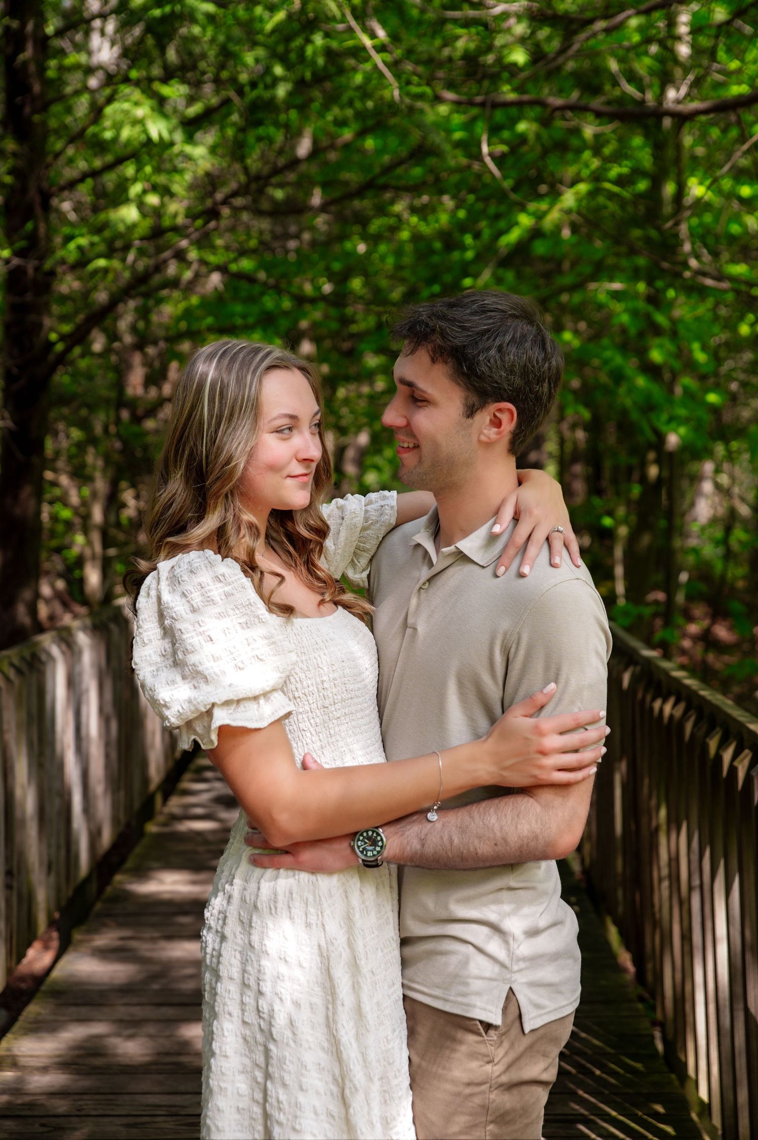Couple shares an intimate moment on a wooden boardwalk surrounded by green foliage.
