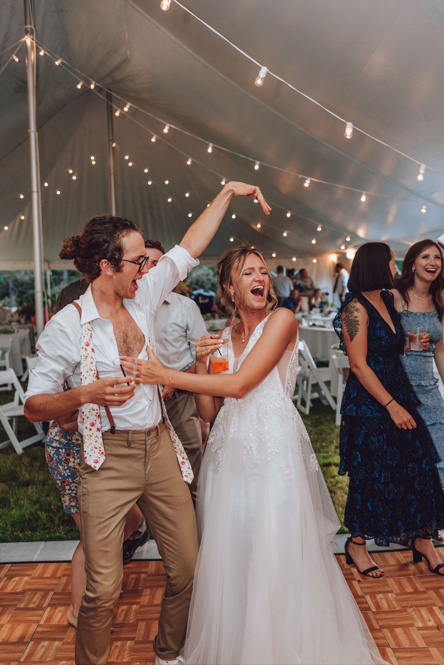 A joyful dance moment under string lights at an outdoor wedding reception.
