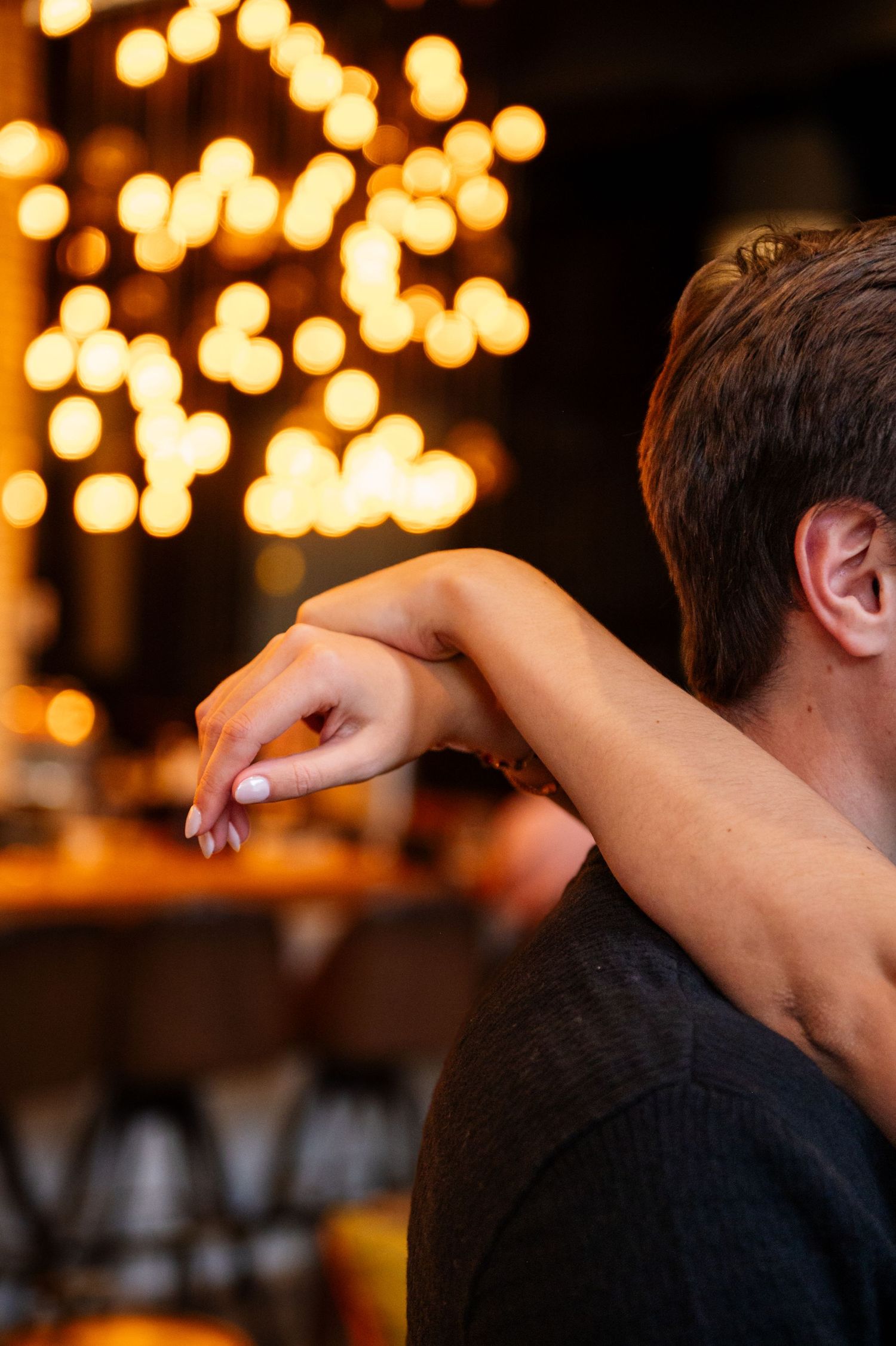 Couple embracing in a romantic bar setting with warm bokeh lights in the background.