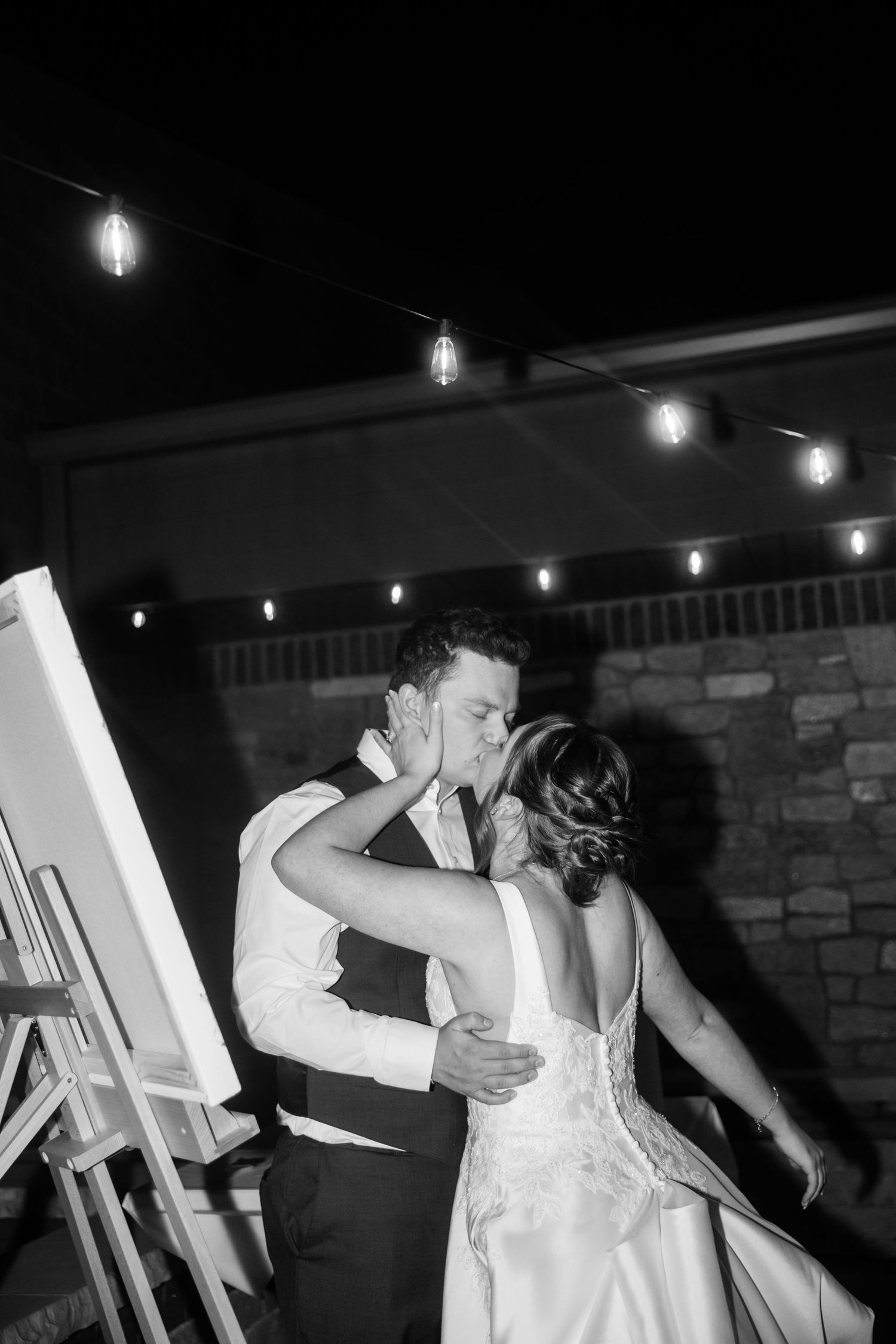A couple shares a romantic dance under twinkling string lights at an evening wedding reception.