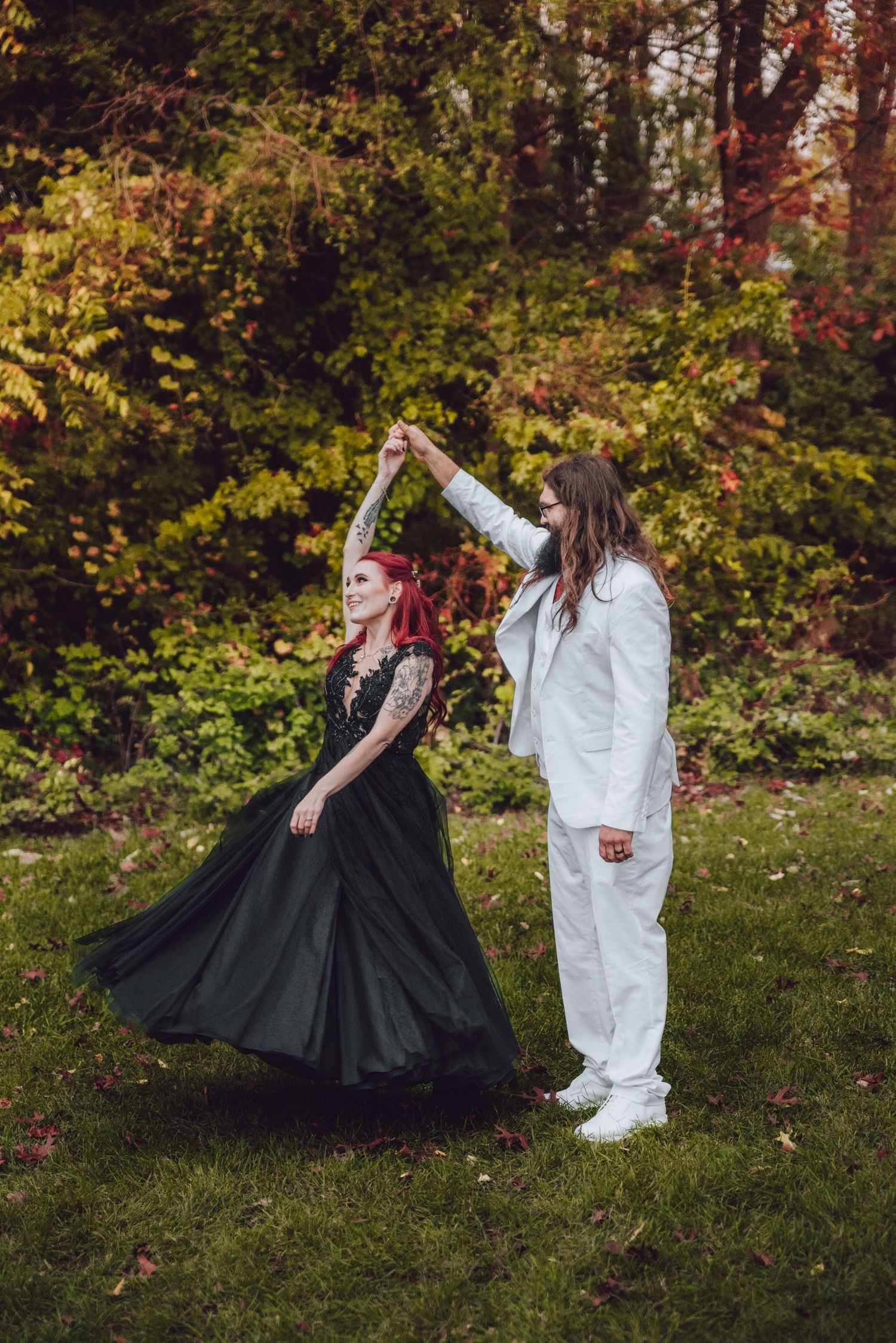 Two people in contrasting black and white outfits dance playfully together on an autumn lawn with colorful fall foliage.