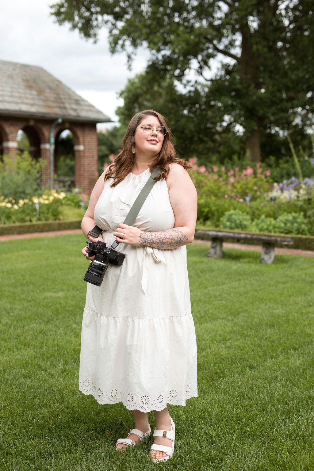 A person in a white lace dress sits on green grass while holding a camera on a sunny summer day.