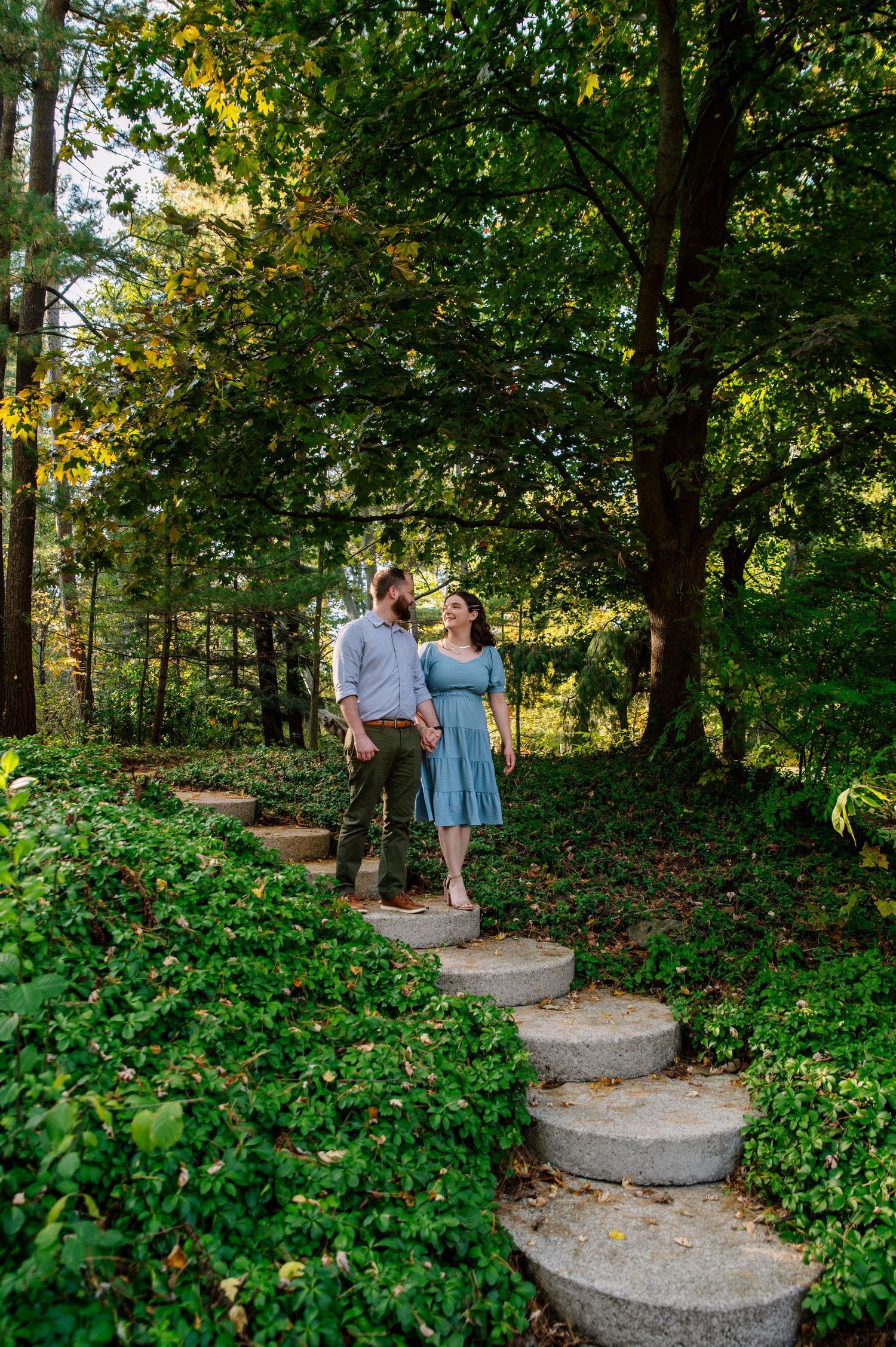 Couple standing on stone garden steps surrounded by lush green landscaping in afternoon sunlight.