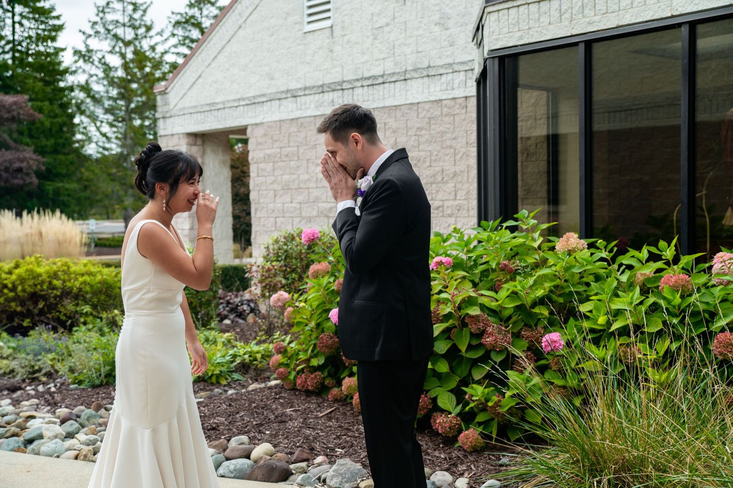 A couple in wedding attire shares a tender moment in a garden setting with lush greenery and flowers.