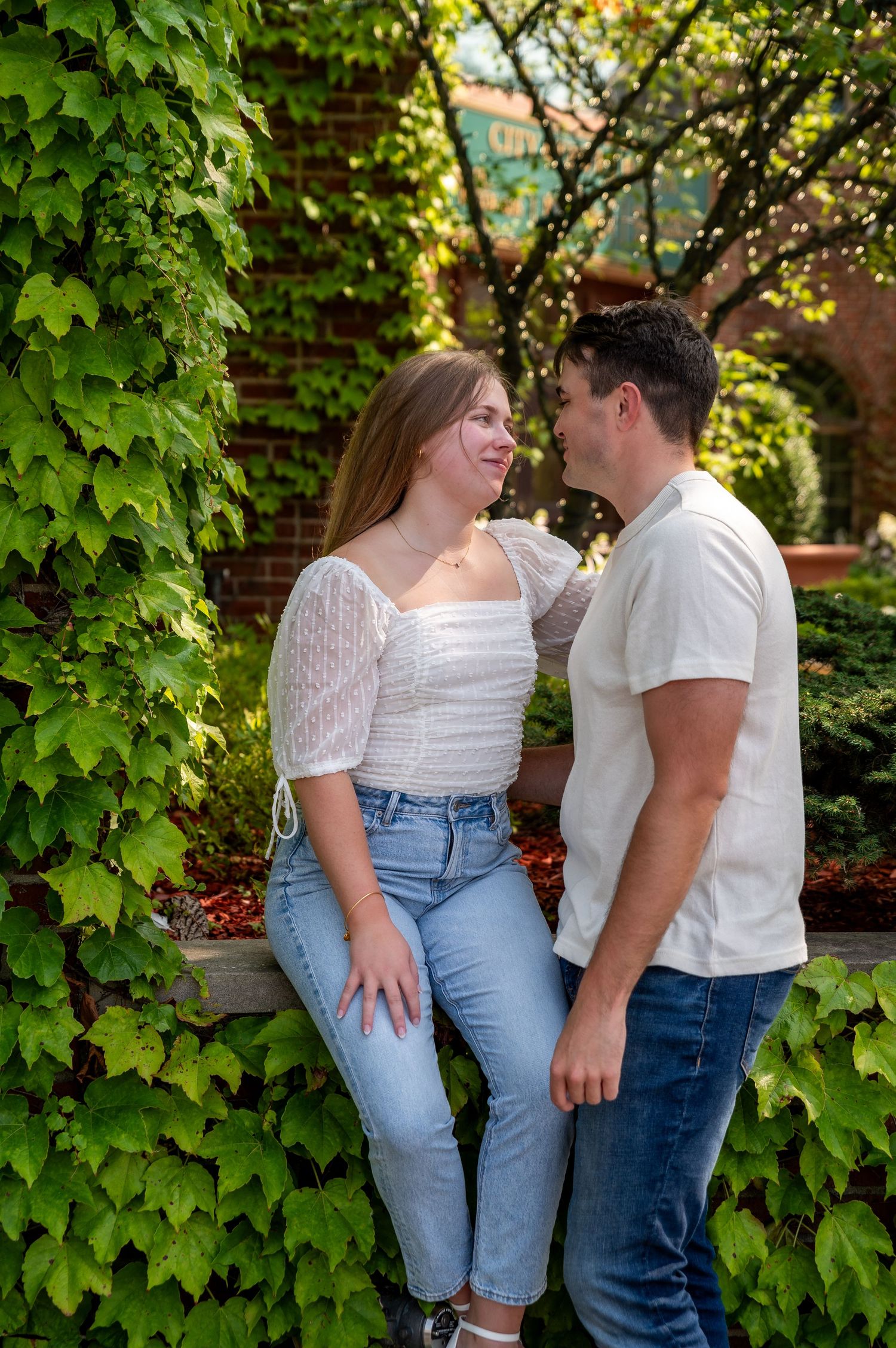 A couple poses against a wall of green ivy on a sunny afternoon.