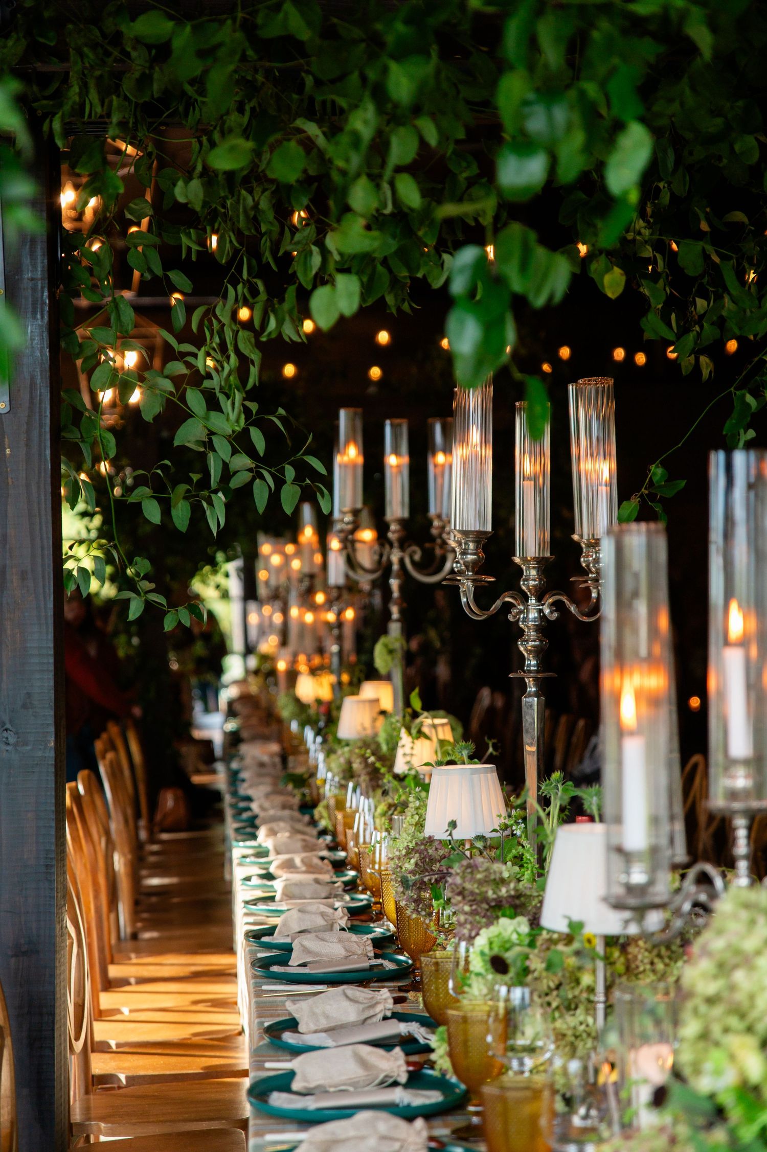 Elegant outdoor dining table set with candelabras, string lights and greenery for a romantic garden wedding reception.