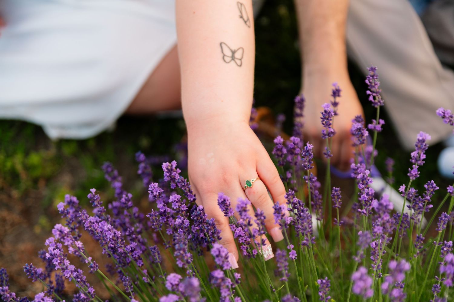 Close-up of hands with butterfly tattoos touching purple lavender flowers.