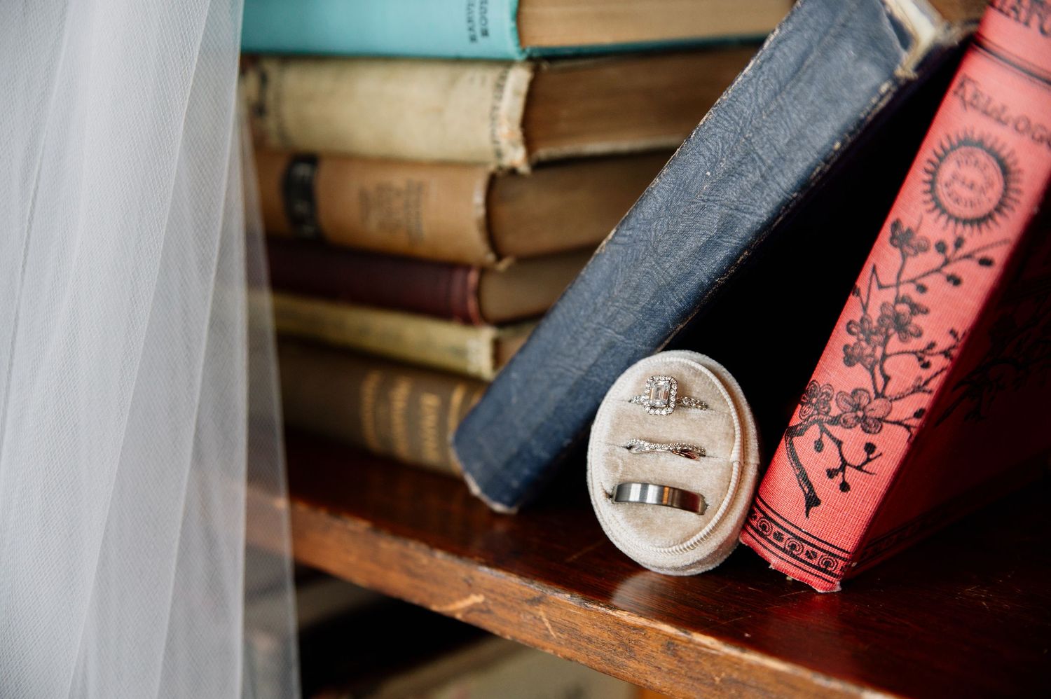 Vintage books on wooden shelf with tulle fabric in soft natural lighting.