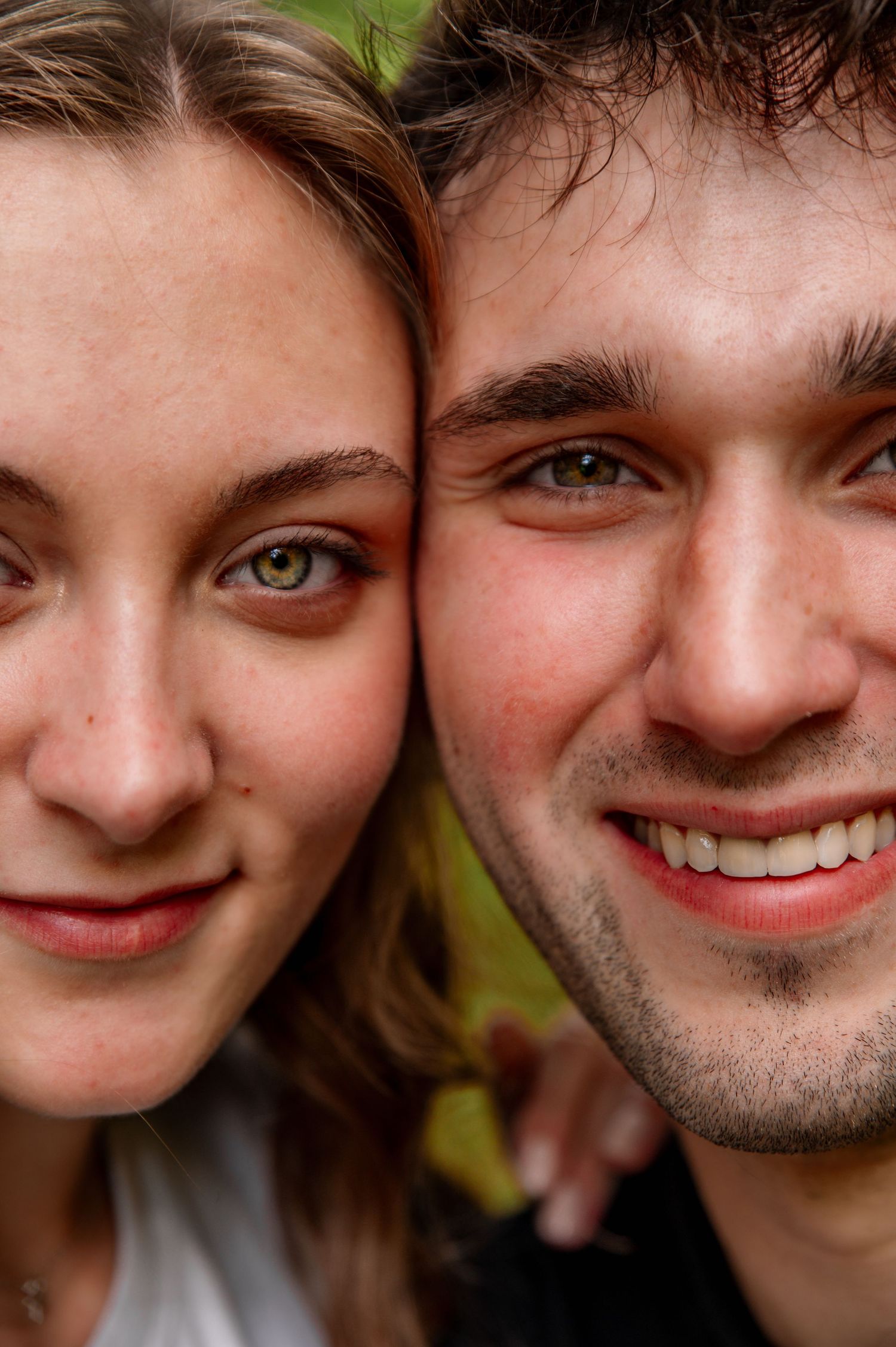 A close-up portrait of a happy couple with bright smiles against a natural background.