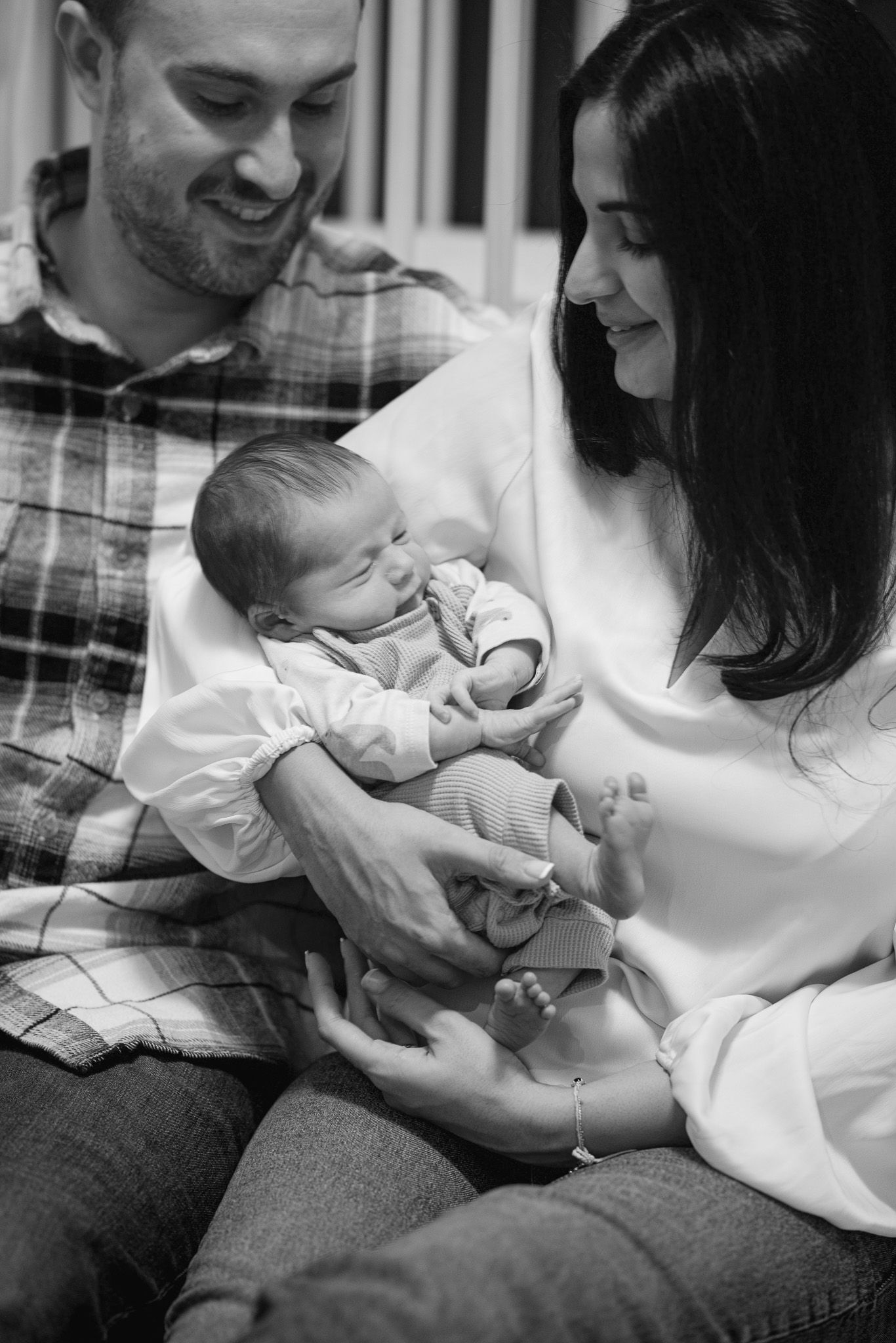 Black and white photo series showing tender moments between parents and their newborn baby on a couch.
