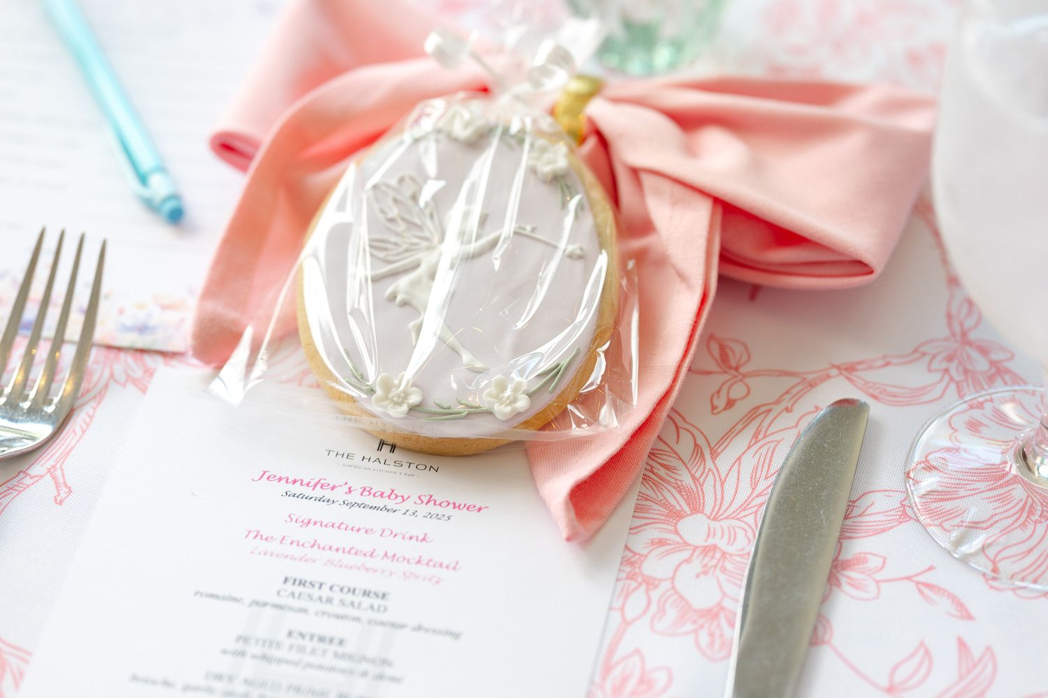 Elegant table setting with pink napkins, silverware, and delicate floral toile pattern details on white linens.