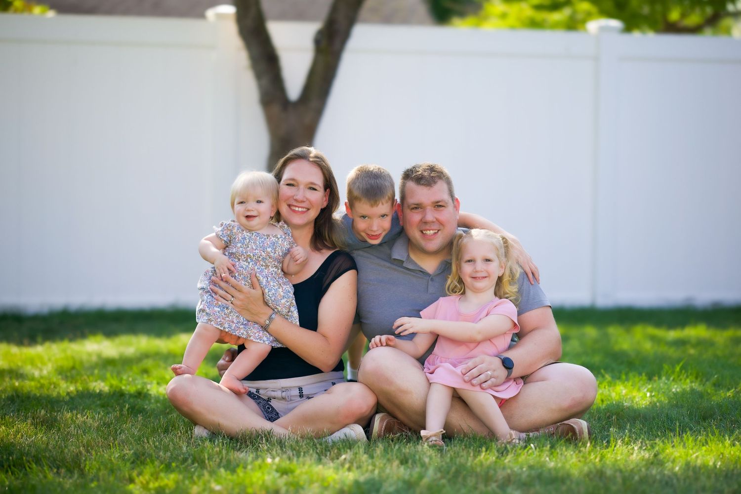 A happy family sits together on green grass in their backyard on a sunny day.