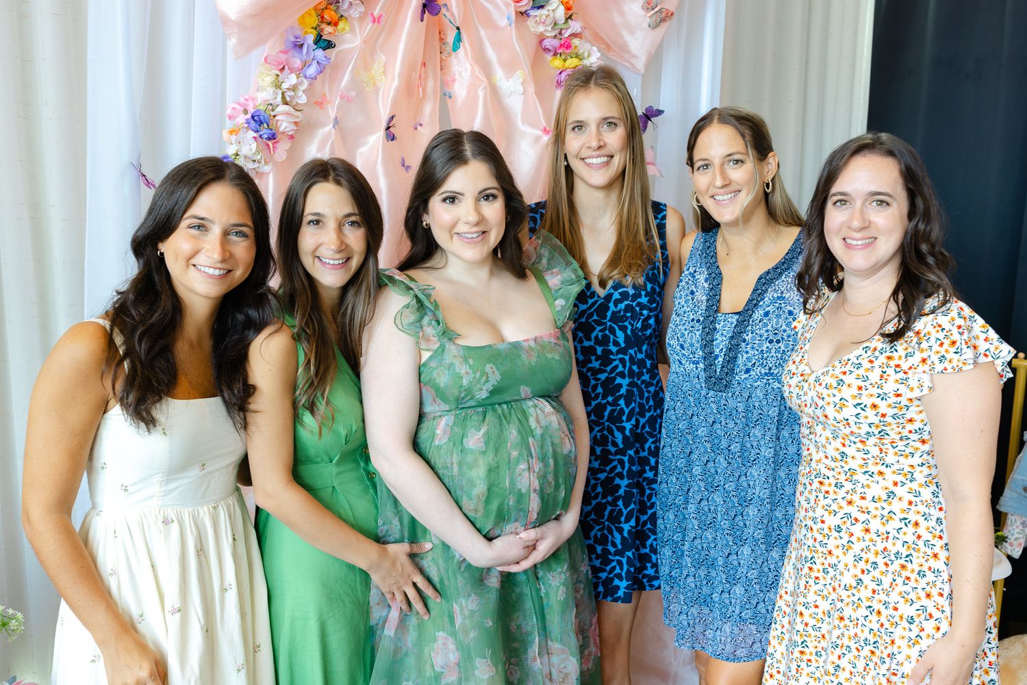 Group of friends in summer dresses pose together at a gathering, with one wearing a green maternity dress.