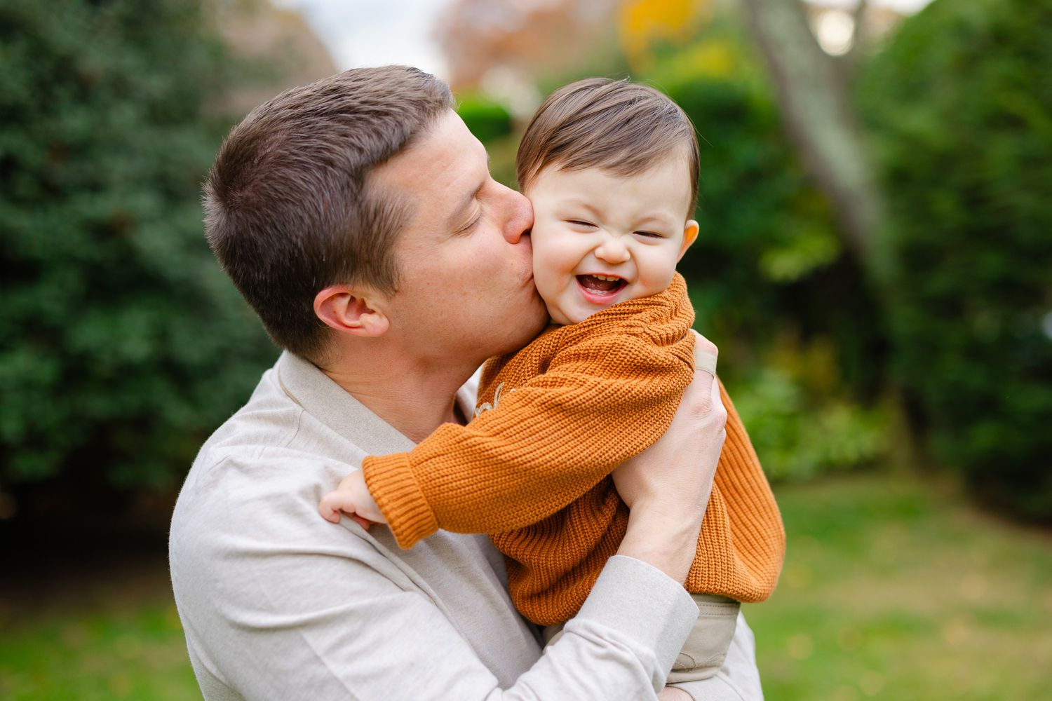 A parent shares a tender moment with their child in a lush green garden setting.