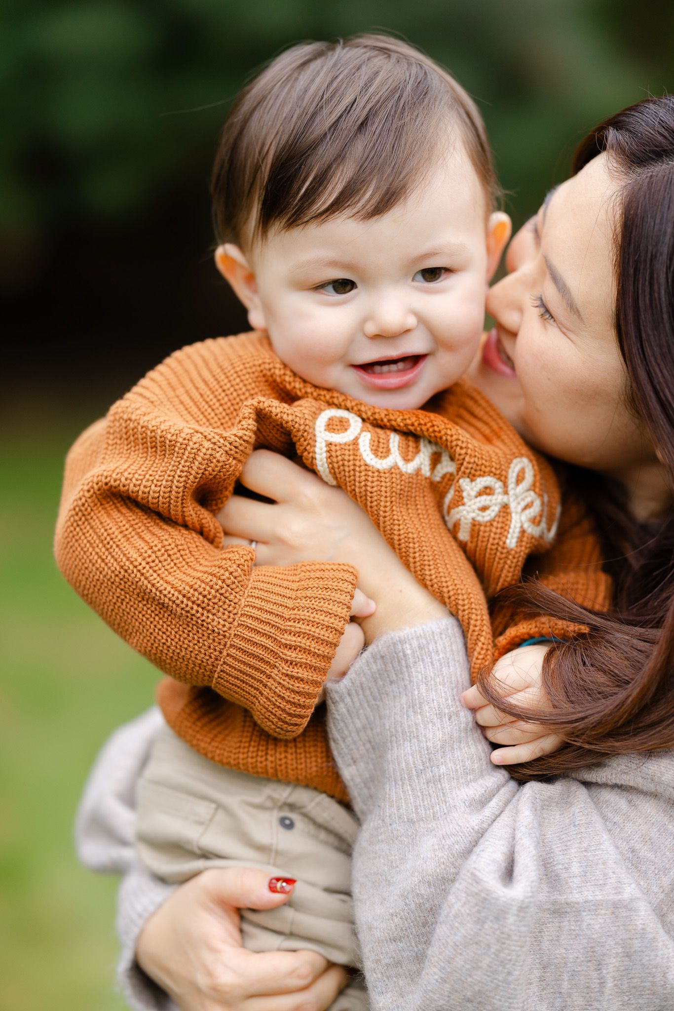 A tender moment between parent and child wearing an orange knit sweater in an outdoor setting.