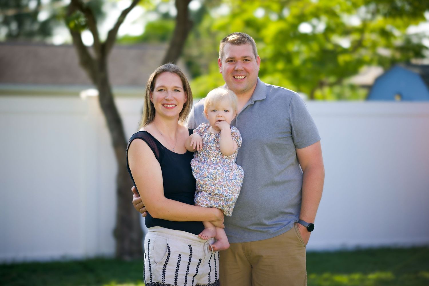 A joyful family gathering poses together in a sunny outdoor setting with lush green foliage in the background.