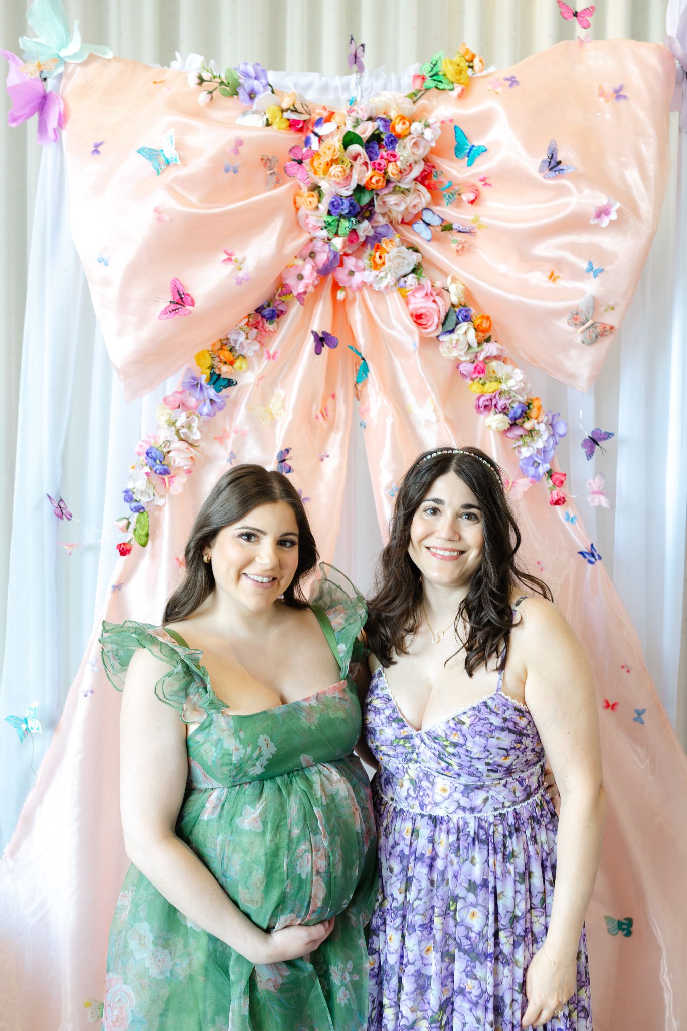 People in green and purple dresses pose in front of a pink backdrop decorated with colorful butterflies.