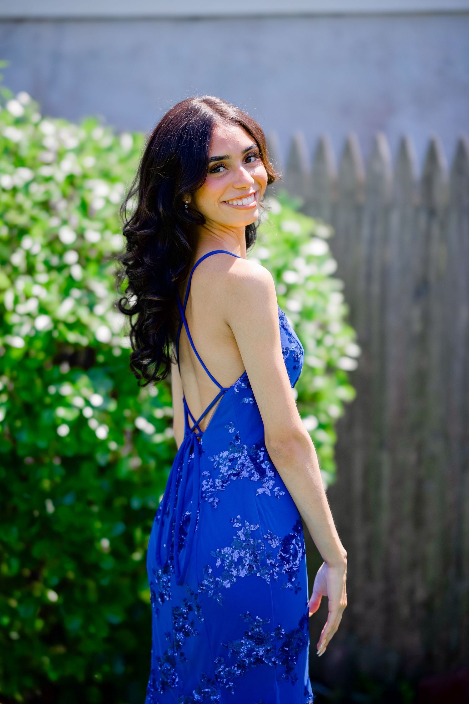 Beautiful flowing blue floral dress with strappy back details photographed in a garden setting with greenery.