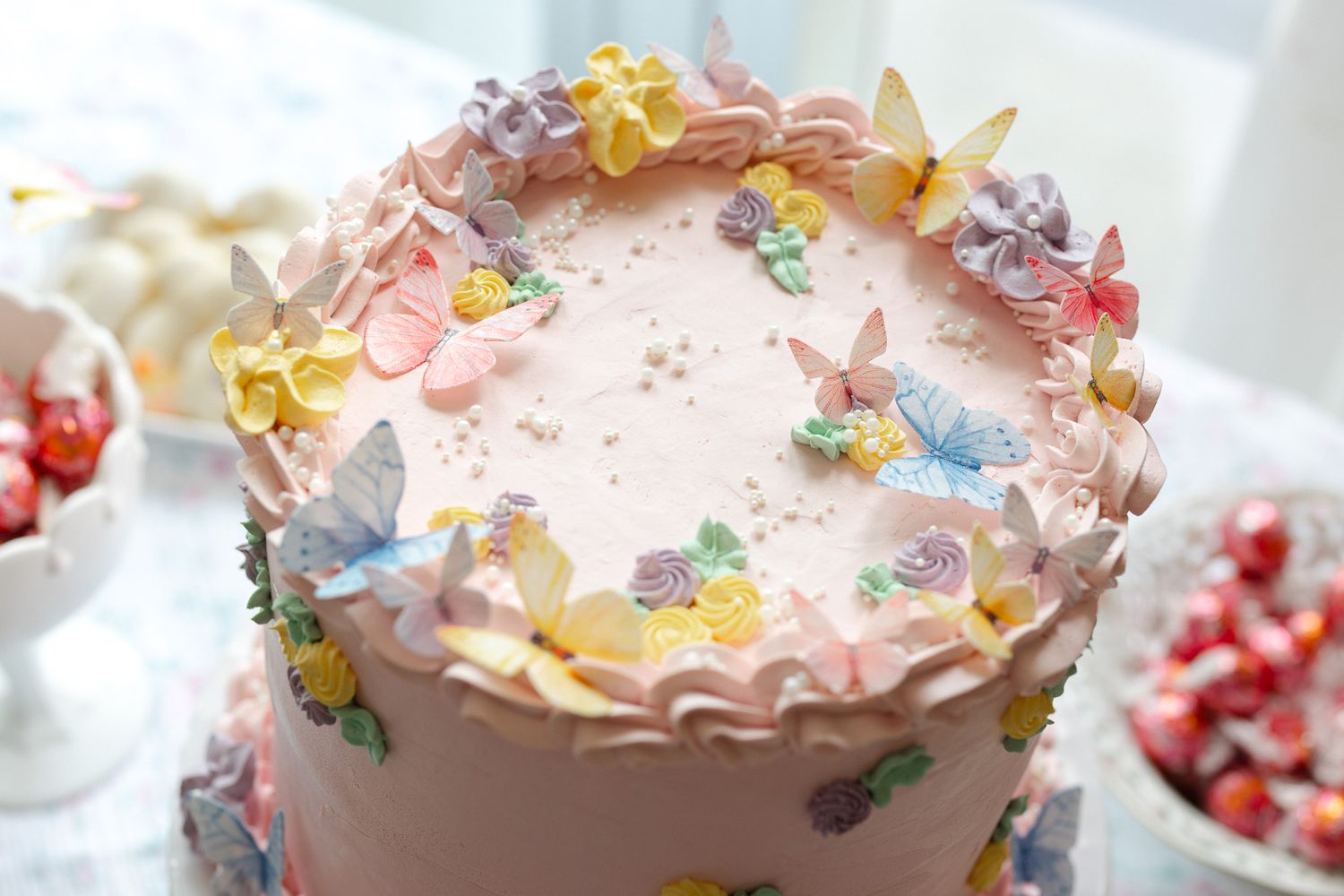 Pink frosted cake decorated with delicate pastel butterflies and floral accents on white background.
