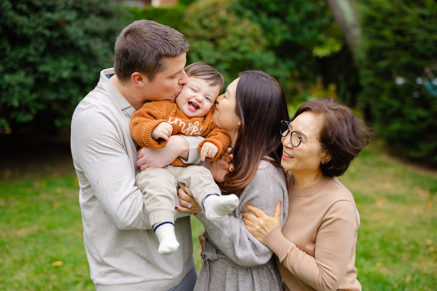 A happy family shares tender moments together outdoors in a natural green setting during a photo session.