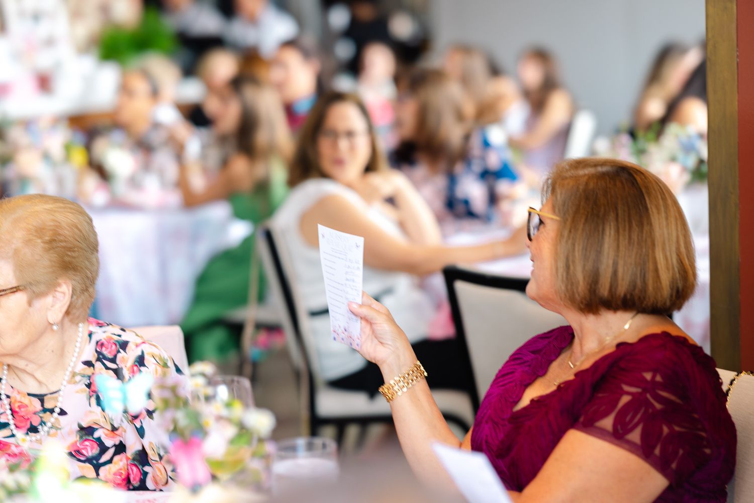 People gathered around tables at a social event with pink decorations and floral arrangements.