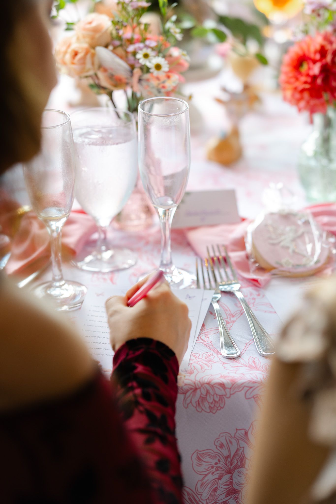 Festive holiday table setting with pink linens and crystal glasses decorated with candy cane striped straws.