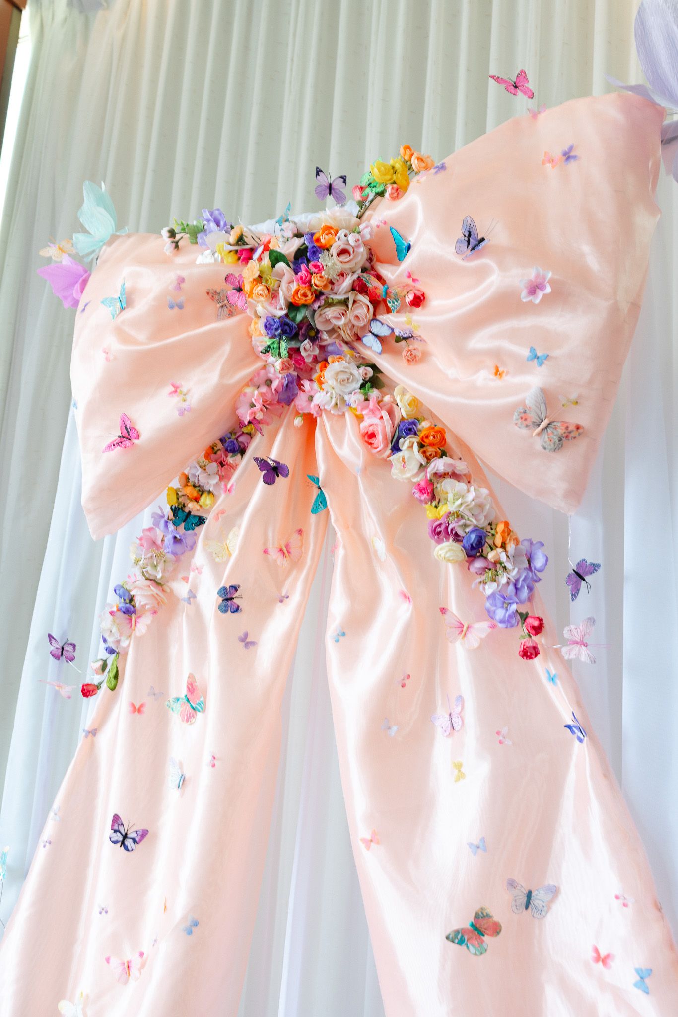 Delicate pink satin bows adorned with colorful butterfly embellishments line a white curtain backdrop.