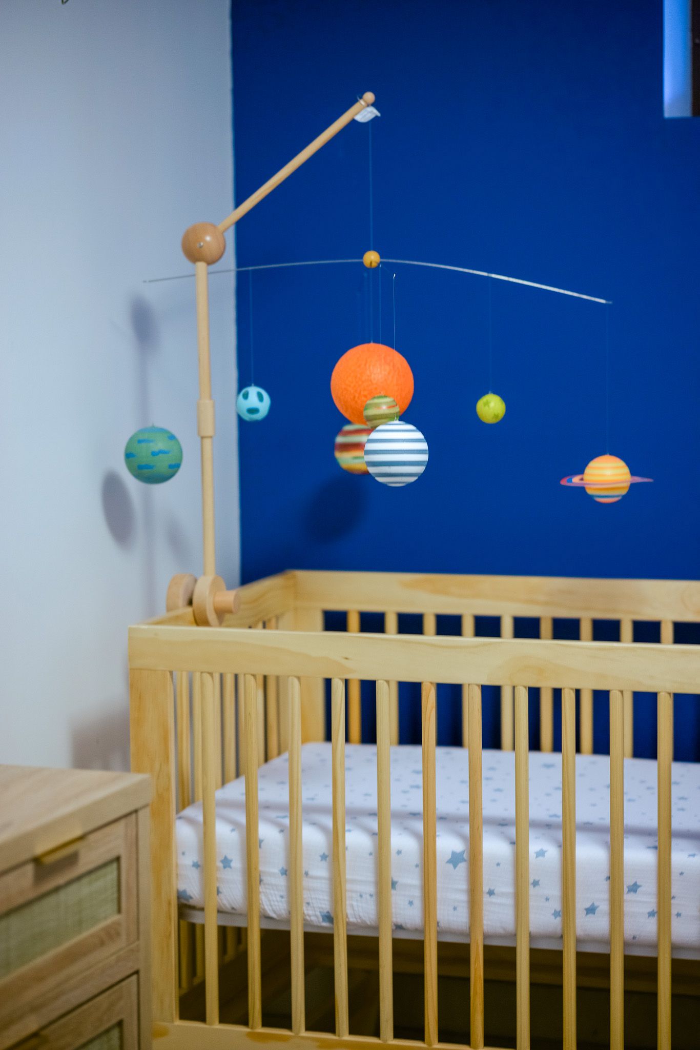 A wooden crib with a colorful solar system mobile hanging above featuring planets and stars against a blue wall.