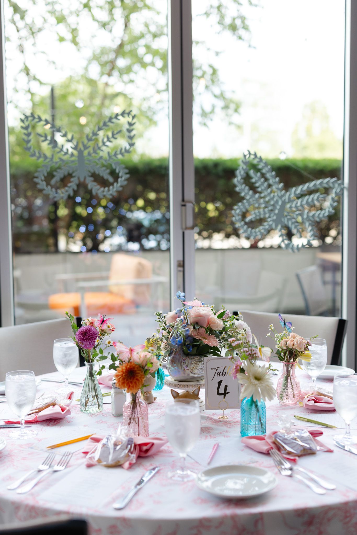 Elegant table setting with pink and blue mason jar flower centerpieces and place settings in a sunlit room.