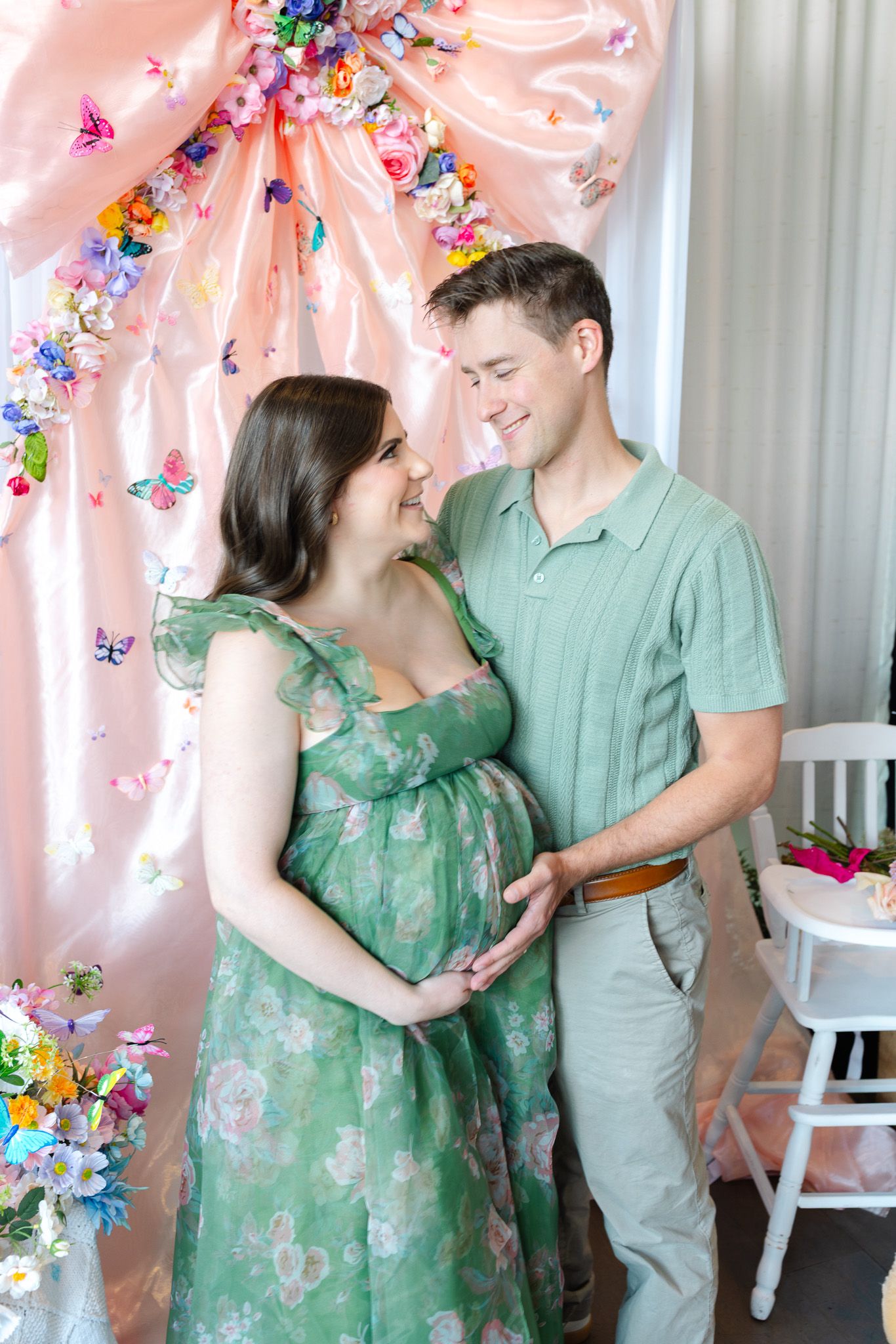 A couple shares tender moments in front of a pink backdrop decorated with colorful butterflies and flowers.