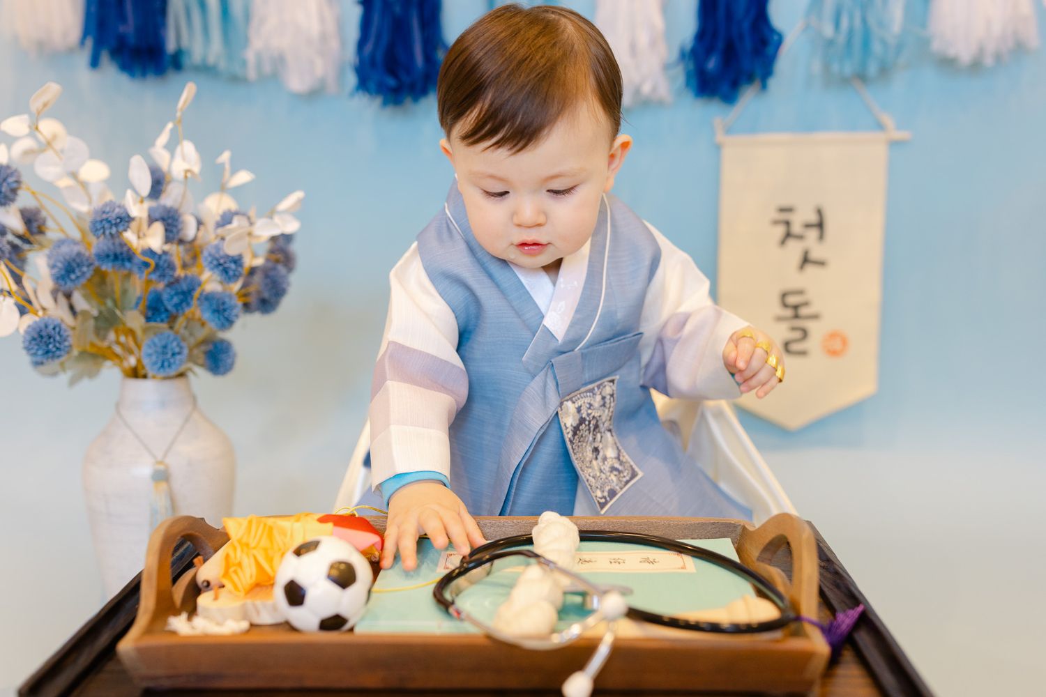 A young child in traditional Korean hanbok clothing plays with decorative paper fans and flowers in a studio setting.