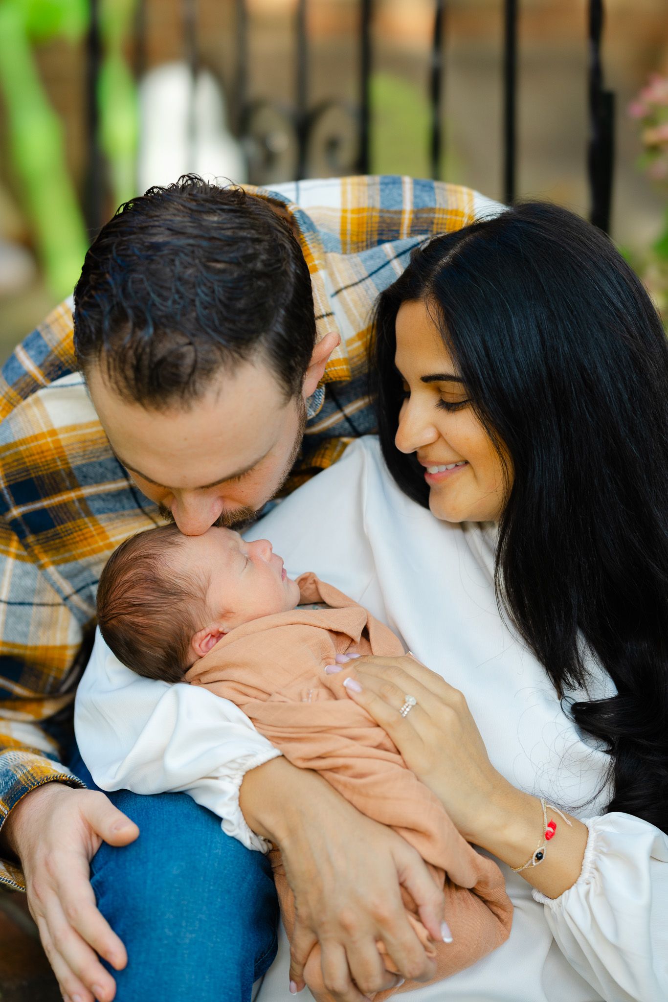 A couple holds and gazes at a baby in a peaceful outdoor setting.