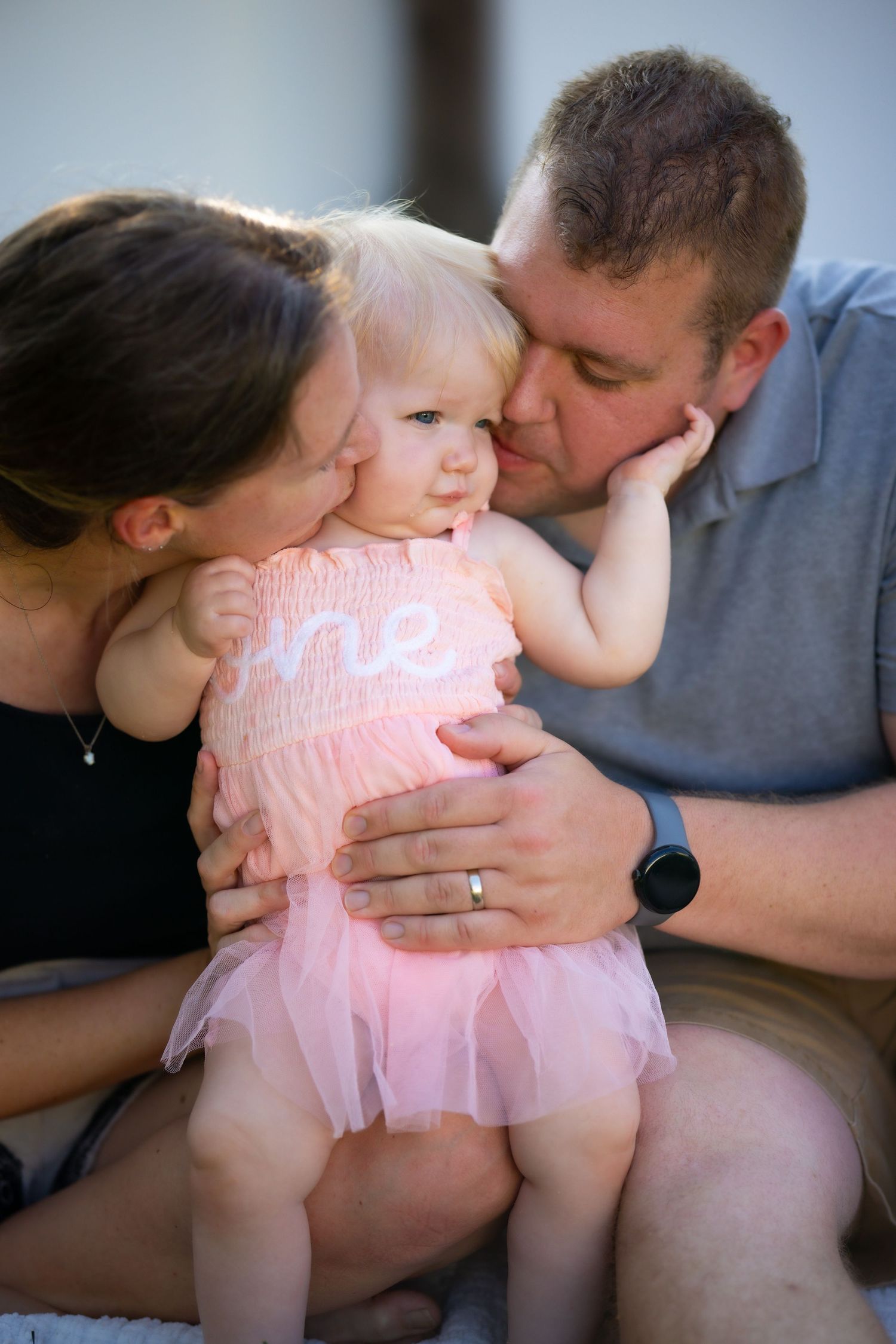 Parents sharing tender kisses with a baby wearing a pink tulle dress.