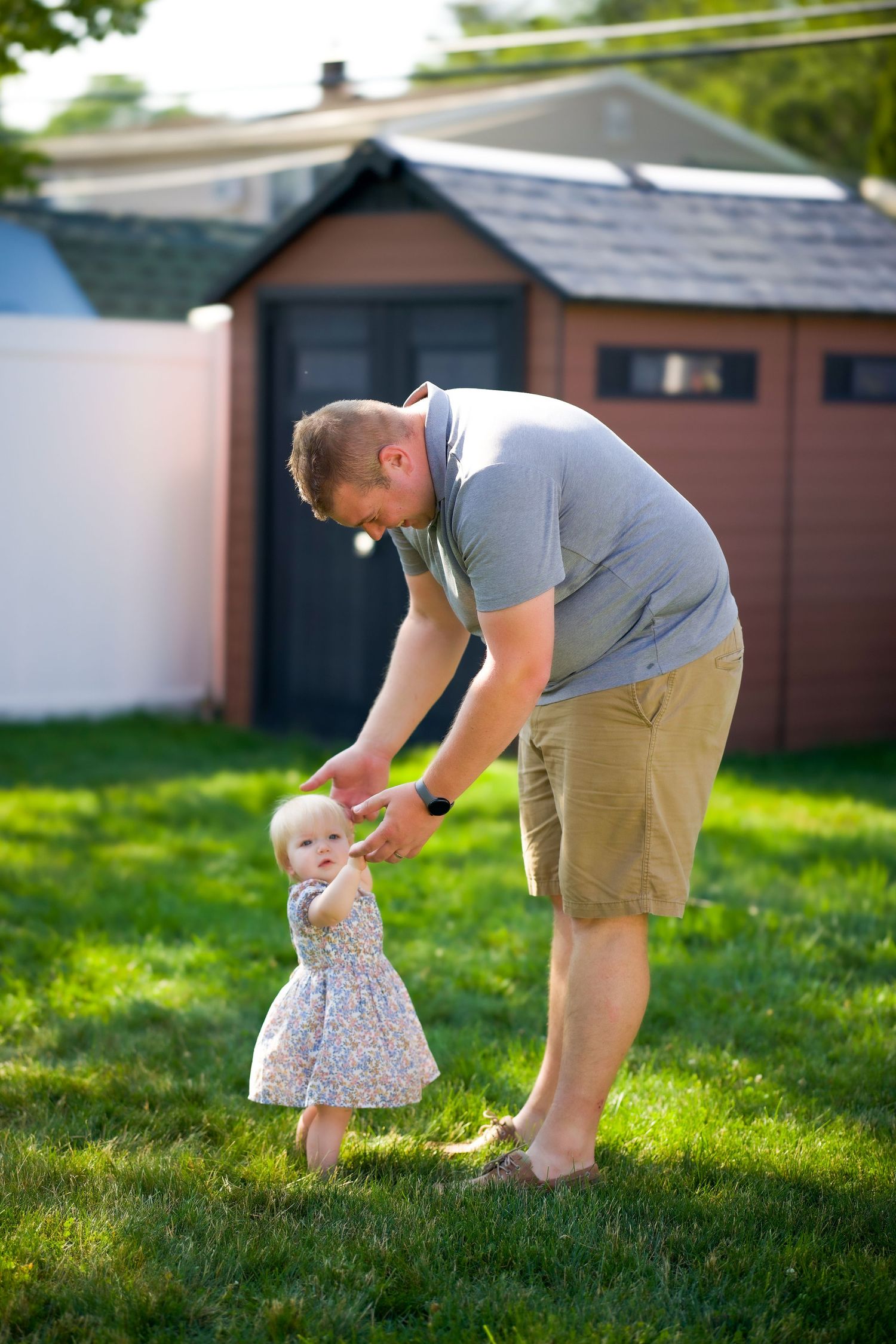 A sweet outdoor moment between parent and small toddler playing together in a backyard with shed in background.