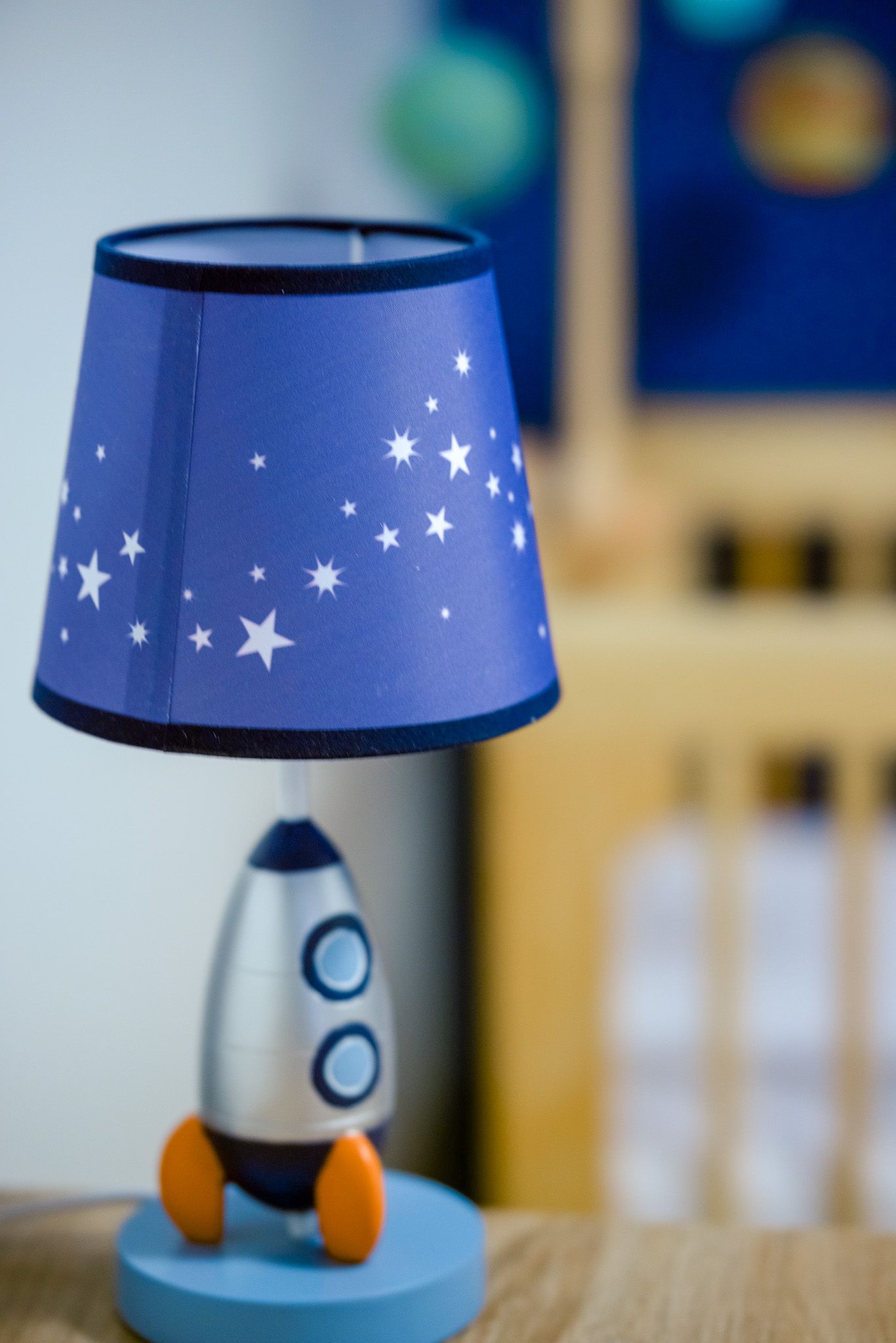 A blue and silver rocket-shaped night light with white stars decorates a nursery shelf.